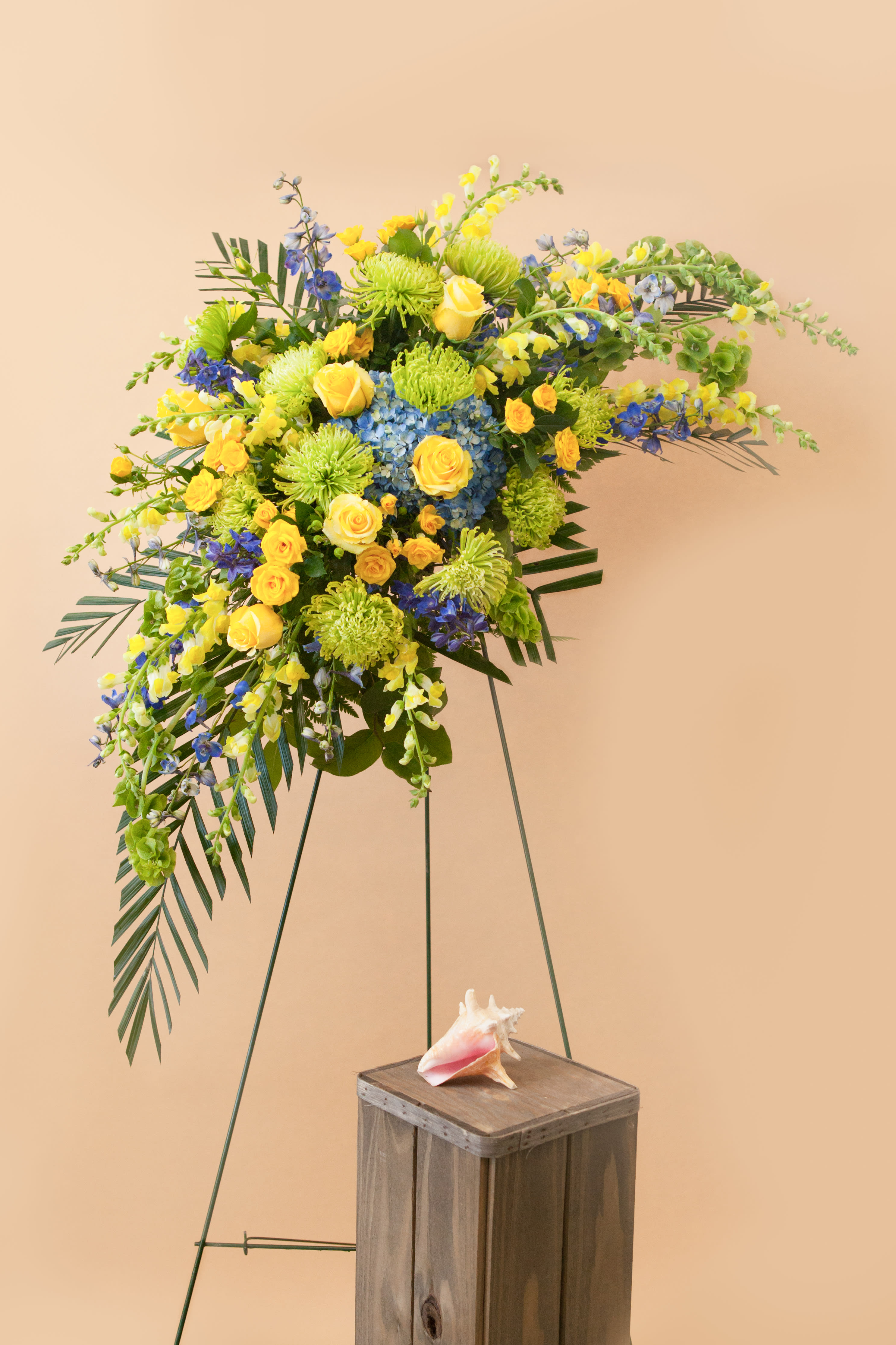 Heavenly Touch - A beautiful loosely crescent shaped standing easel service arrangement shown in yellows, blues and greens- but can be customized to your color preference. Flowers will be chose to match your color palette. Delivered with a standing easel frame. Flowers may vary based on seasonality and availability.  Please call if this is a concern.