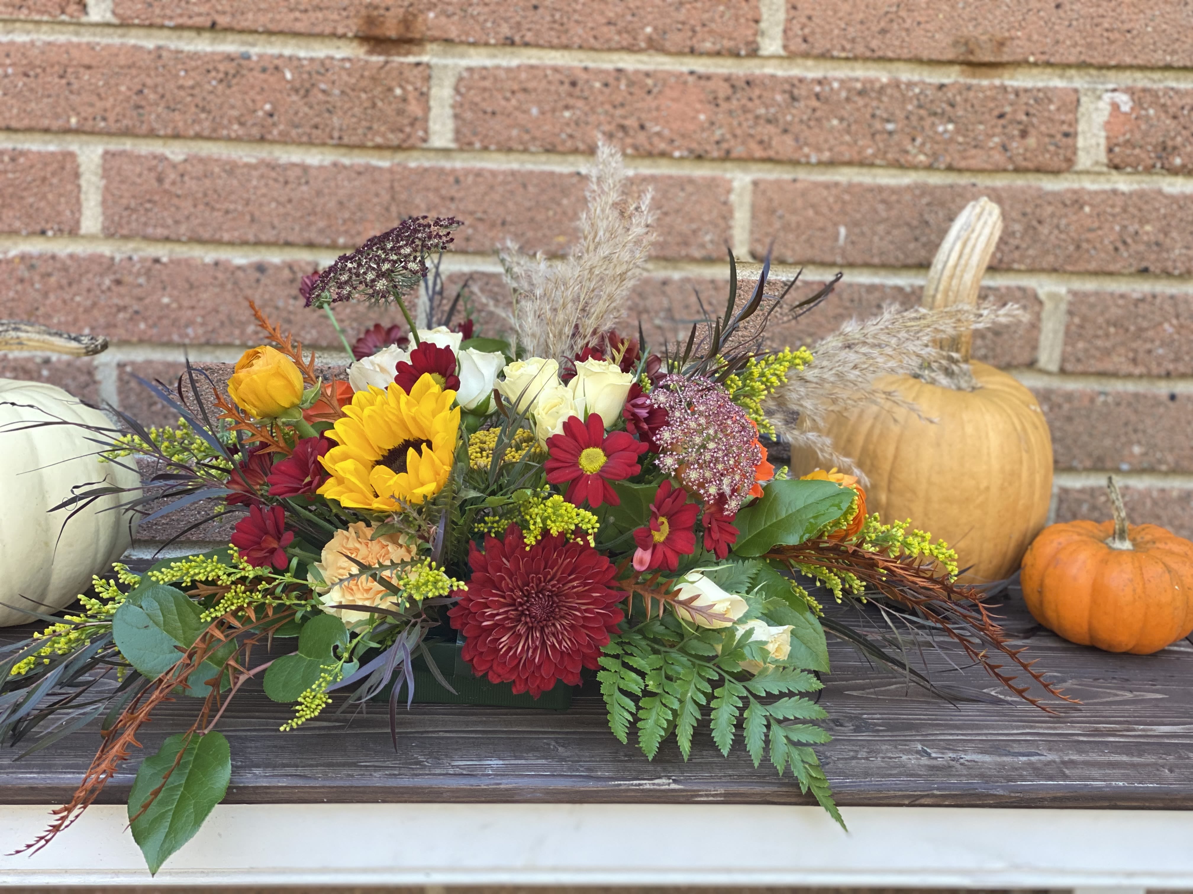 Thanksgiving Centerpiece Arrangement  - The designer will select only the best flowers of the day to create FALL THEMED arrangement or bouquet inspired by the seasonal beauty of the flowers. A Standard arrangement  is in a floral dish.  Deluxe and Premium arrangements are in glass cube containers.   PLEASE NOTE: The flower selection in the picture is for the design sample and to represent the sizes. The selection of the the flower and color schemes will vary due to seasonal availability.