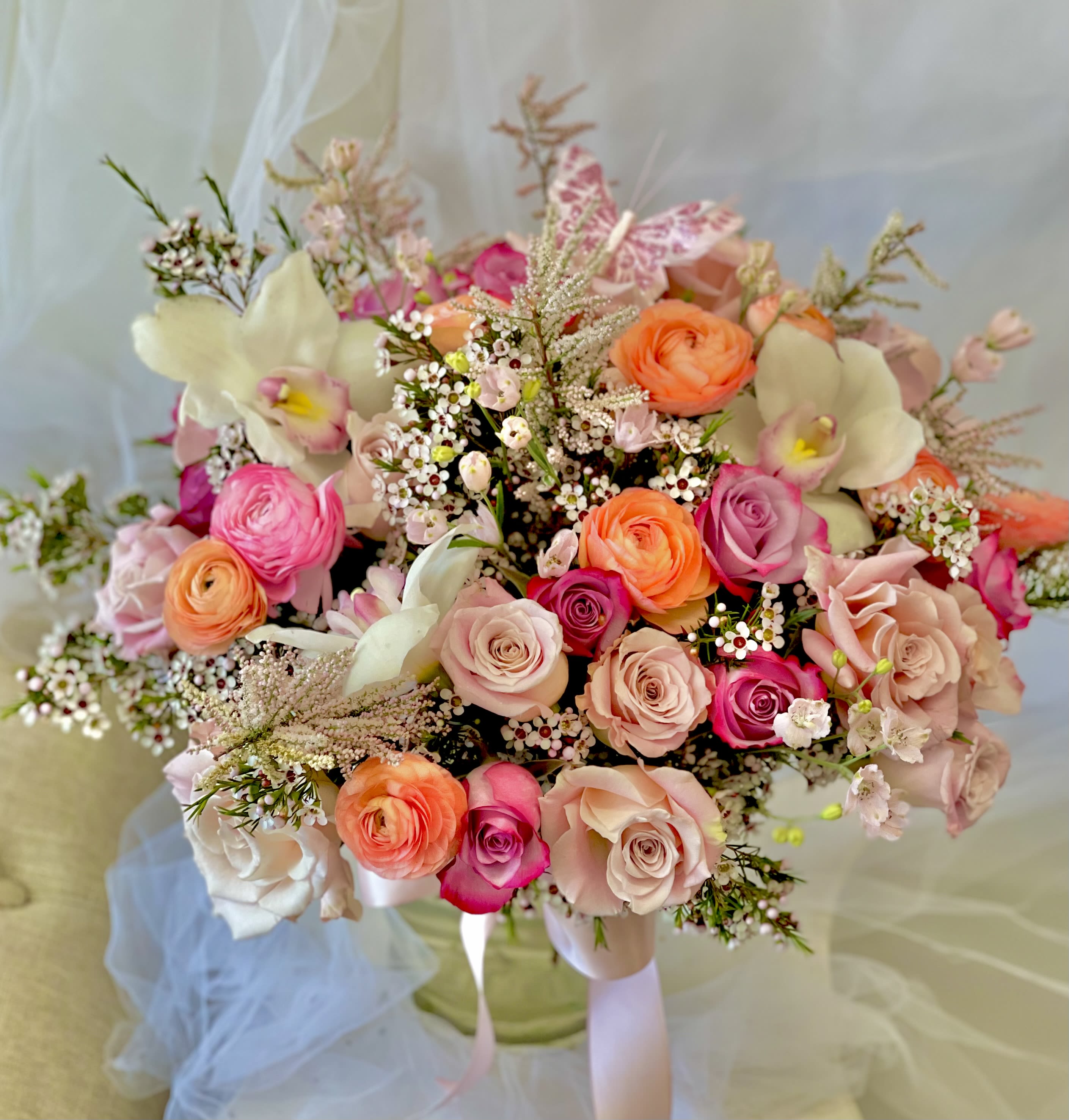 Pink Butterfly - Theme Colors: Shades of pinks, peaches and purple, White.  Featured Blooms: Roses, Spray Roses, Seasonal Blooms, Orchid , Ranunculus, Delphinium, Wildflowers.  HK Flowers have a uniqueness of florals and seasonal blooms, certain flowers or colors may not be available as each season affects the availability, color, size, and shape of each floral bloom. Some flowers may be substituted accordingly.  Photos are used as a reference for the color palette and is NOT indicated of the final product. We ask for your trust in us that we will pick out the best seasonal available blooms, while still capturing the arrangements theme and colors mentioned above.  