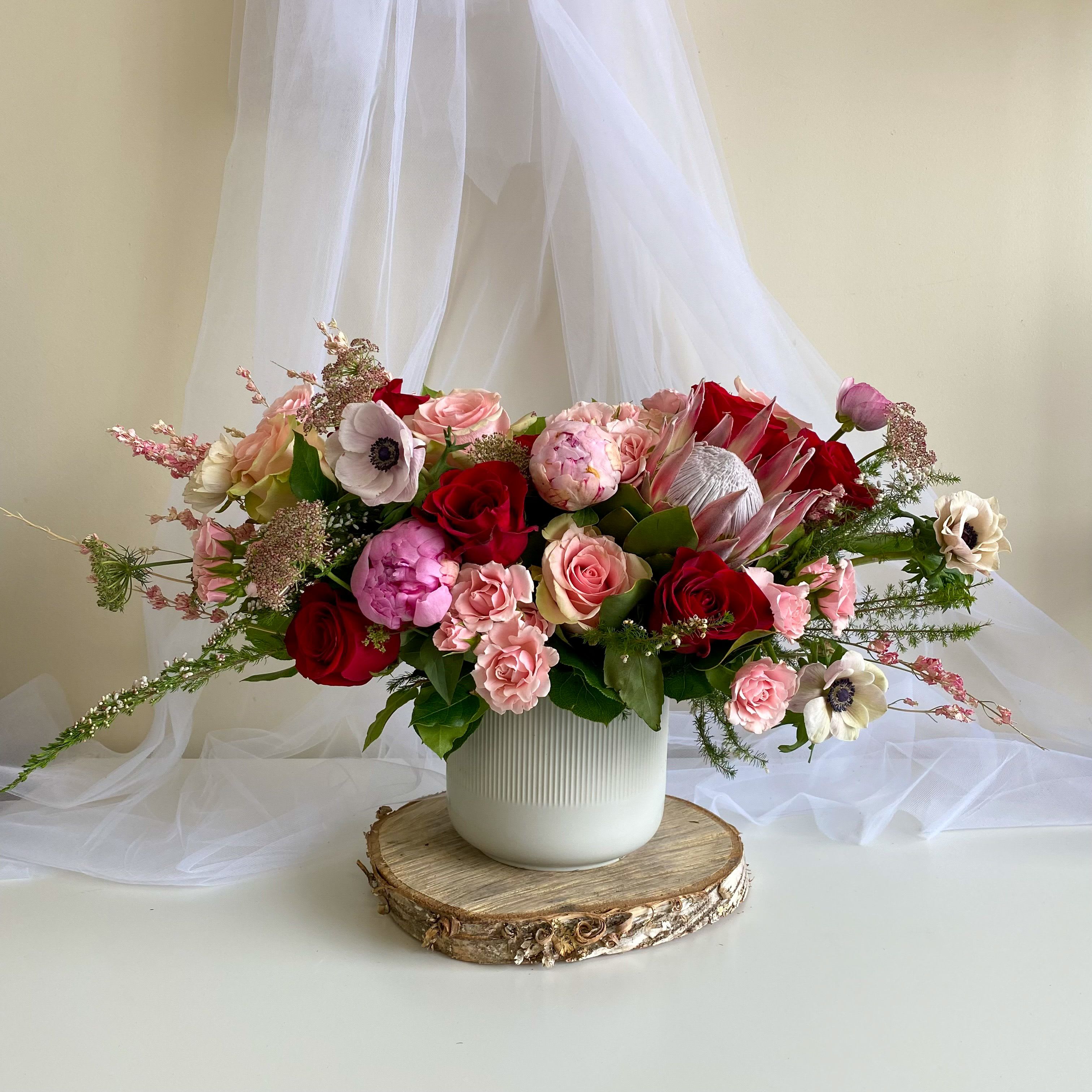 Romance Romance - Theme Colors: Shades of pinks with reds Featured Blooms: Roses, Peonies, Protea, poppy anemone, with Seasonal Blooms HK Flowers have a uniqueness of florals and seasonal blooms, certain flowers or colors may not be available as each season affects the availability, color, size, and shape of each floral bloom. Some flowers may be substituted accordingly. Photos are used as a reference for the color palette and is NOT indicated of the final product. We ask for your trust in us that we will pick out the best seasonal available blooms, while still capturing the arrangements theme and colors mentioned above.