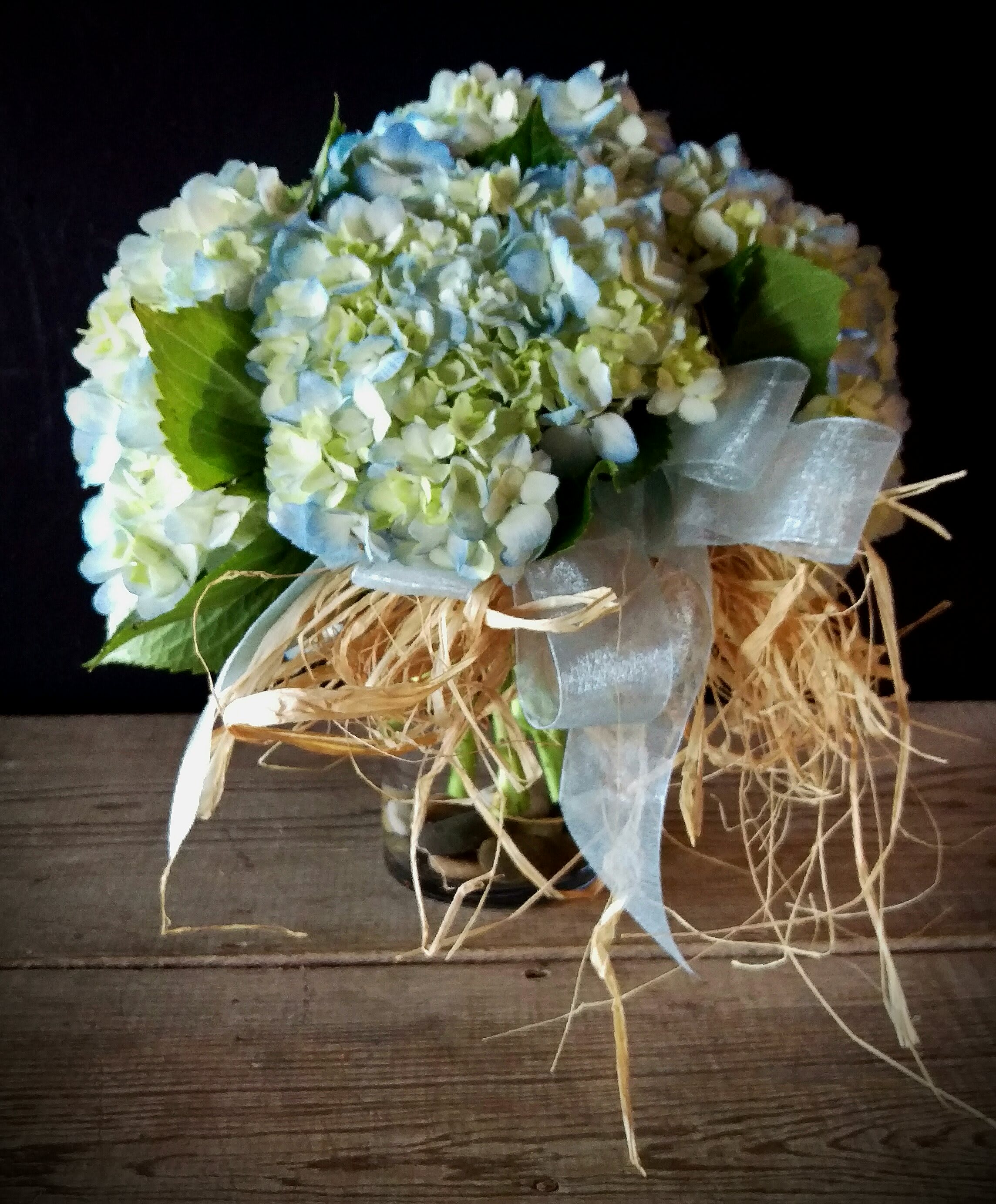 Carnton Hydrangea Cluster in blue Carnton Hydrangea Cluster in blue - Inspired by the hydrangeas that line the fences near the gardens of Carnton Plantation in Franklin, Tennessee... this design features pale blue hydrangeas, hand gathered and clustered together and place in a simple vase on a bed of riverstones.. accented with a simple ribbon and raffia.