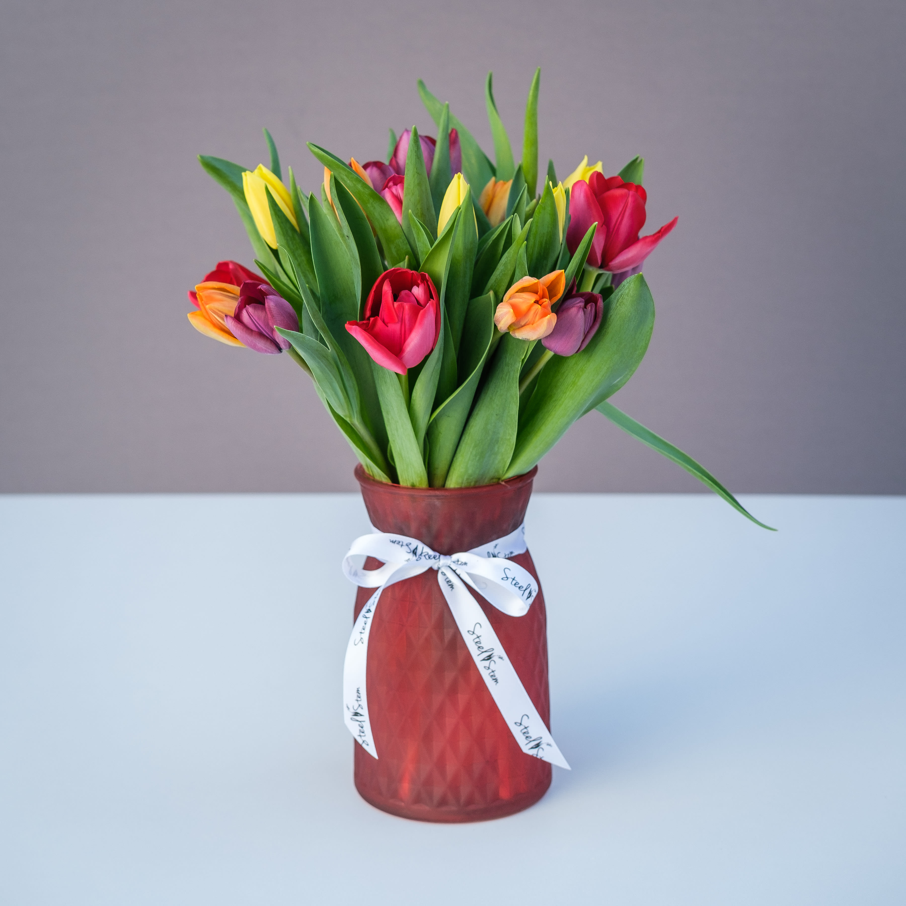 My Tulip My Tulip - A vibrant and cheerful mixture of colorful tulips that are happily arranged into a red glass vase with our signature Steel Stem ribbon. Watch these tulips grow over time and celebrate in style!
