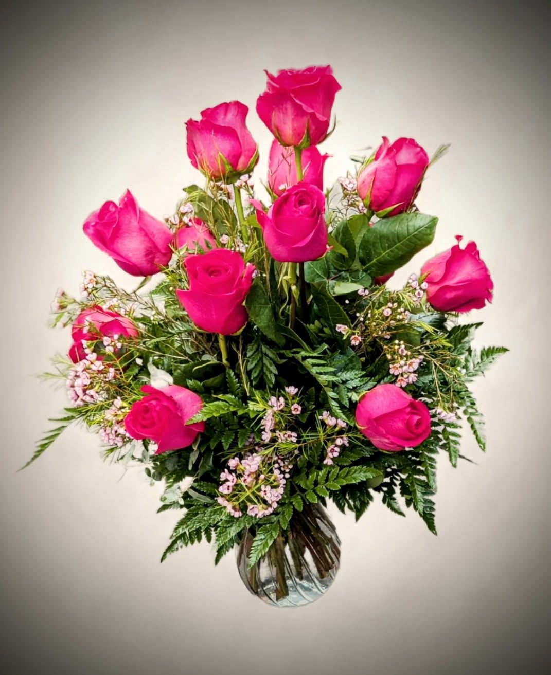 Bold elegance rose vase  - A classic statement of love and admiration, the Bold Elegance Rose Vase features 12 vivid hot pink roses accented with delicate filler flowers and lush greenery. Arranged in a clear glass vase, this striking bouquet brings passion and charm to any celebration or heartfelt gesture. 