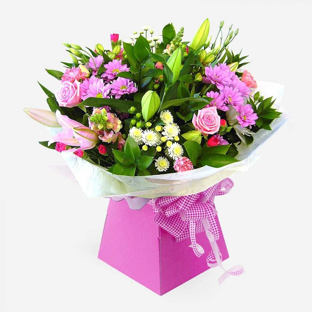 Ashleigh - Brighten someone’s day with this stunning hand-tied bouquet presented in a charming pink gift box. This delightful arrangement features a lovely mix of seasonal blooms in soft and vibrant shades of pink, white, and green.  Flowers Included: 	•	Pink Roses 	•	Lilies (Pink and unopened buds) 	•	Pink Chrysanthemums 	•	White Spray Chrysanthemums 	•	Lisianthus (buds) 	•	Carnations (pink) 	•	Seasonal greenery and filler flowers  Perfect for birthdays, anniversaries, or simply to show someone you care.