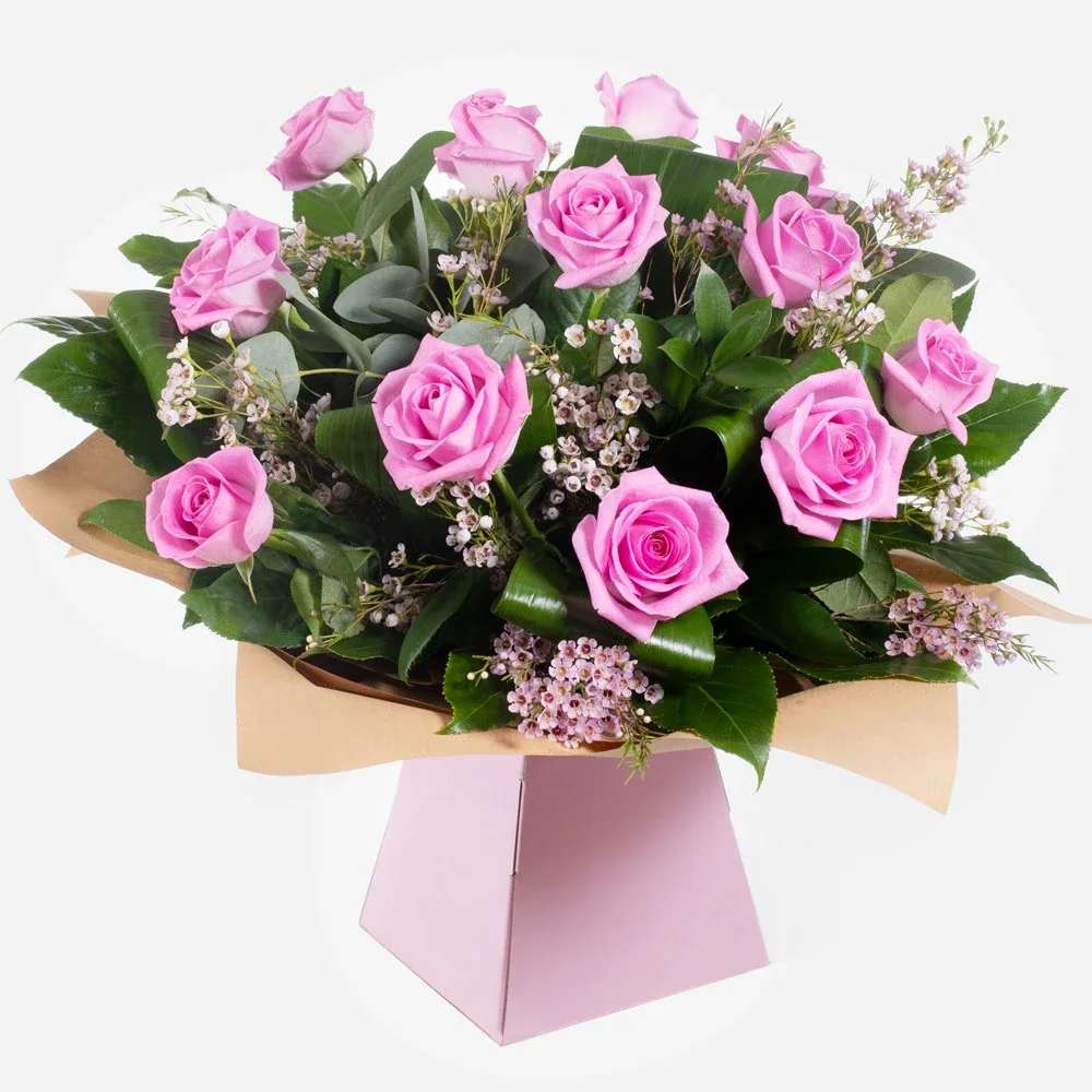 Dreamy Dozen - The bouquet in the image features a lovely and elegant arrangement with the following flowers: 	•	Pink Roses 	•	Waxflowers (small light pink/white flowers used as fillers) 	•	Assorted Greenery (including broad glossy leaves and other foliage for volume and contrast)  This bouquet has a romantic and delicate look, perfect for anniversaries, Valentine’s Day, or expressing affection.