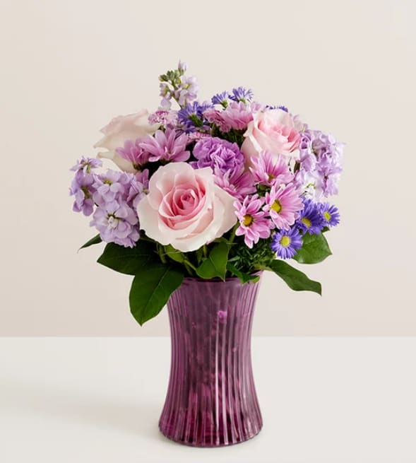 Daydream Bouquet™ - Just like a daydream. Our delightful lavender bouquet is gathered with accents of pink and lush greenery in our striking fluted violet gathering vase. Designed in vintage pressed glass with ribbed detailing, it captures the rich beauty of the blooms, along with the thoughtfulness of your sentiment.  Product Details: All-around arrangement with pink roses; lavender carnations, daisy poms, button poms and stock; purple monte casino; accented with assorted greenery Artistically designed in our exclusive fluted gathering vase in a lovely shade of violet; vintage pressed glass with ribbed detail creates a charming enhancement for the floral arrangement; measures 7.9&quot;H x 5&quot;D Premium arrangement measures approximately 17&quot;H x 14&quot;W Deluxe arrangement measures approximately 15&quot;H x 13&quot;W Standard arrangement measures approximately 14&quot;H x 12&quot;W Our florists hand-design each arrangement, so colors and varieties may vary due to local availability