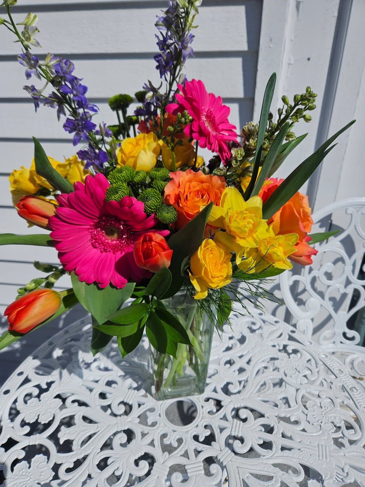 Sherbet Surprise Bouquet - Purple larkspur, hot pink gerbera daisies, orange roses, tulips, daffodils and yellow spray roses arranged in a clear vase