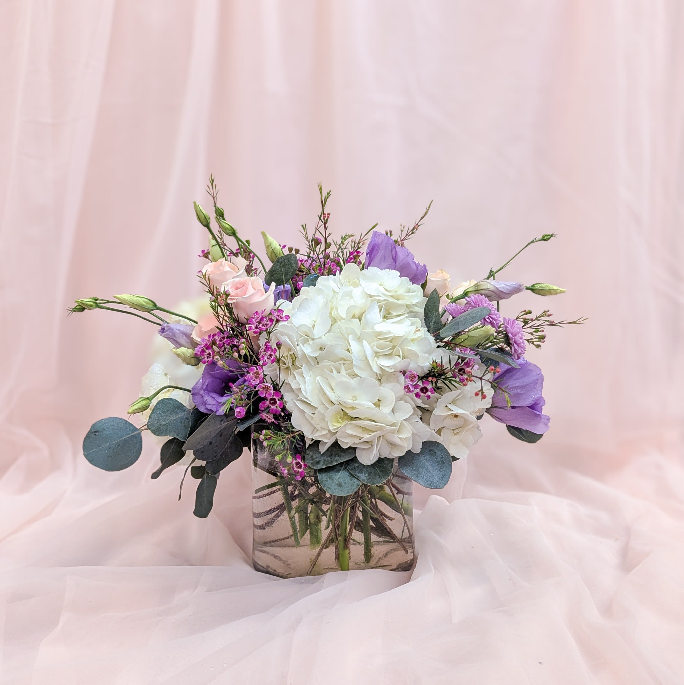 Lavender Bliss Lavender Bliss - A charming arrangement that exudes warmth and elegance. Featuring fluffy white hydrangeas, soft lavender Lisianthus, vibrant purple wax flowers, cheerful button mums, and blush pink spray roses, this bouquet is perfect for welcoming a new baby, celebrating a birthday, or simply brightening someone's day. A delightful gift to spread joy and smiles!