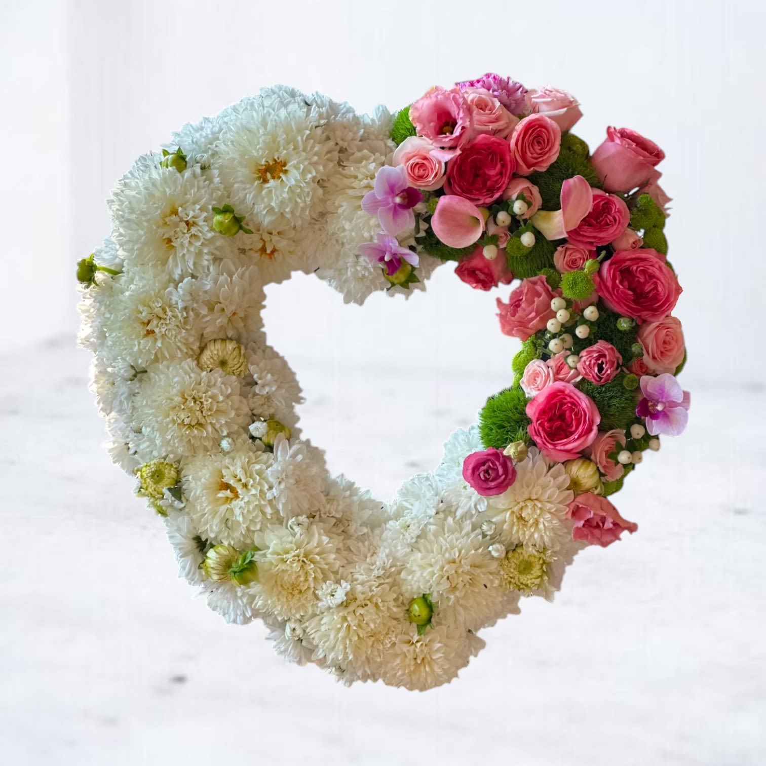 Eternal Love Wreath - Honor cherished memories with the Eternal Love Wreath, a heartfelt floral tribute featuring pure white chrysanthemums arranged in a classic heart shape, accented with vibrant pink garden roses, delicate orchids, and fresh green touches. This elegant wreath symbolizes love, remembrance, and everlasting devotion, offering comfort and beauty at funeral services, memorials, or celebrations of life. Whiskey Wallflower provides same-day delivery in Houston and surrounding areas—order the Eternal Love Wreath today to express your deepest sympathy and love with grace and care.  Easels are included in the price of all wreath arrangements to ensure easy display at services.