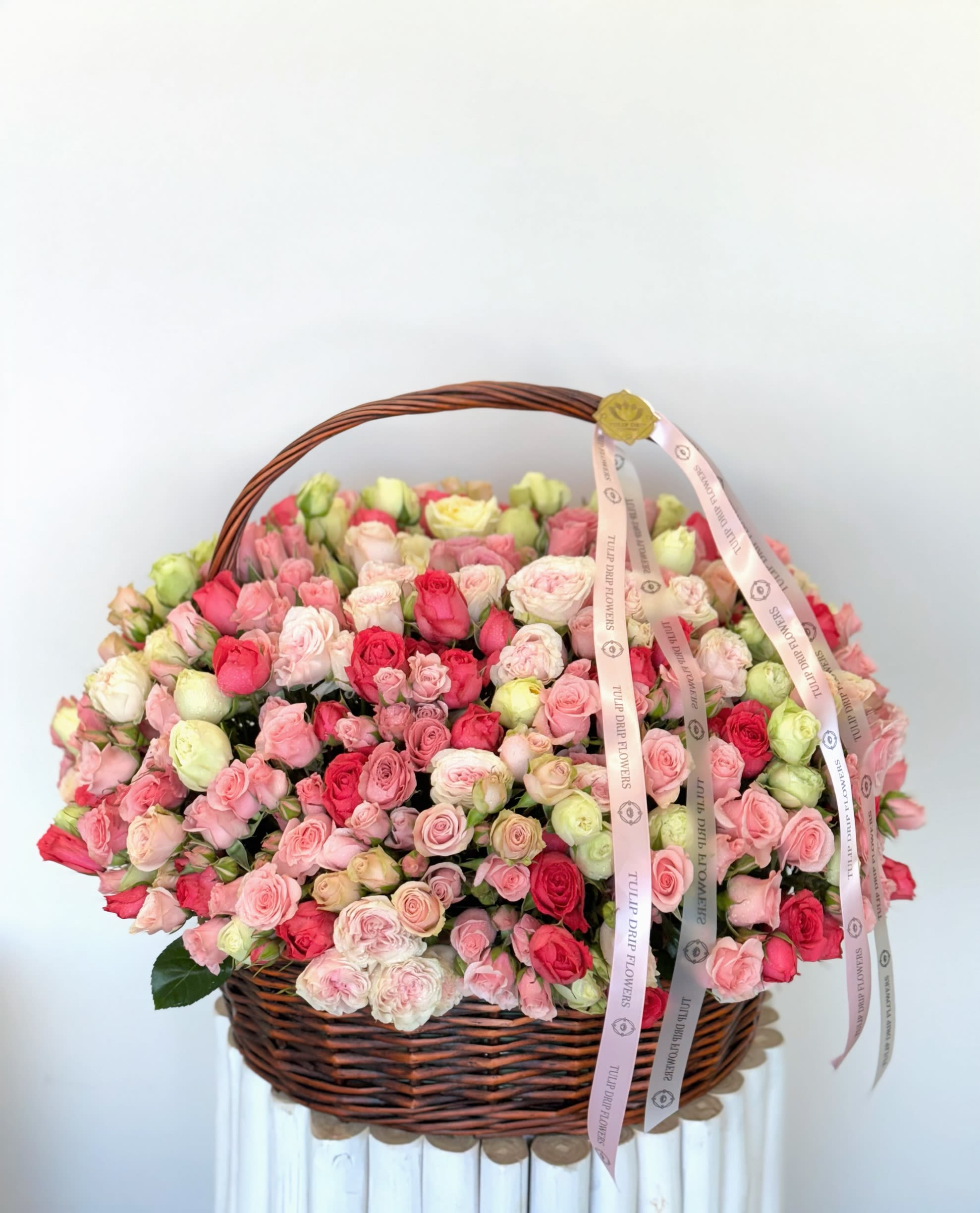 Blushing Garden Basket Blushing Garden Basket - A luxurious wicker basket overflowing with premium spray roses in soft pink, creamy white, and vibrant red hues. This stunning arrangement is perfect for celebrating Mother’s Day with elegance and love.