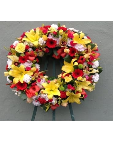 EUROPEAN WREATH - SYM-054 EUROPEAN WREATH - SYM-054 - A beautiful and elegant European-style wreath with orange, white, and yellow flowers on an easel. **Picture shows the deluxe option.