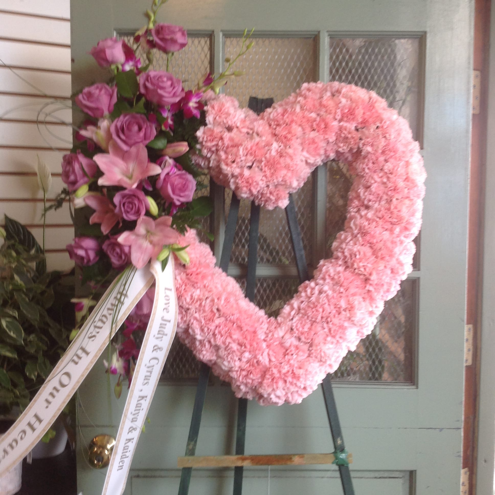 EUROPEAN HEART - Sym-201 EUROPEAN HEART - Sym-201 - A beautiful and elegant European-style wreath in the shape of a heart with pink and purple flowers on an easel. **Price does not include a printed banner. Picture is Premium Size.