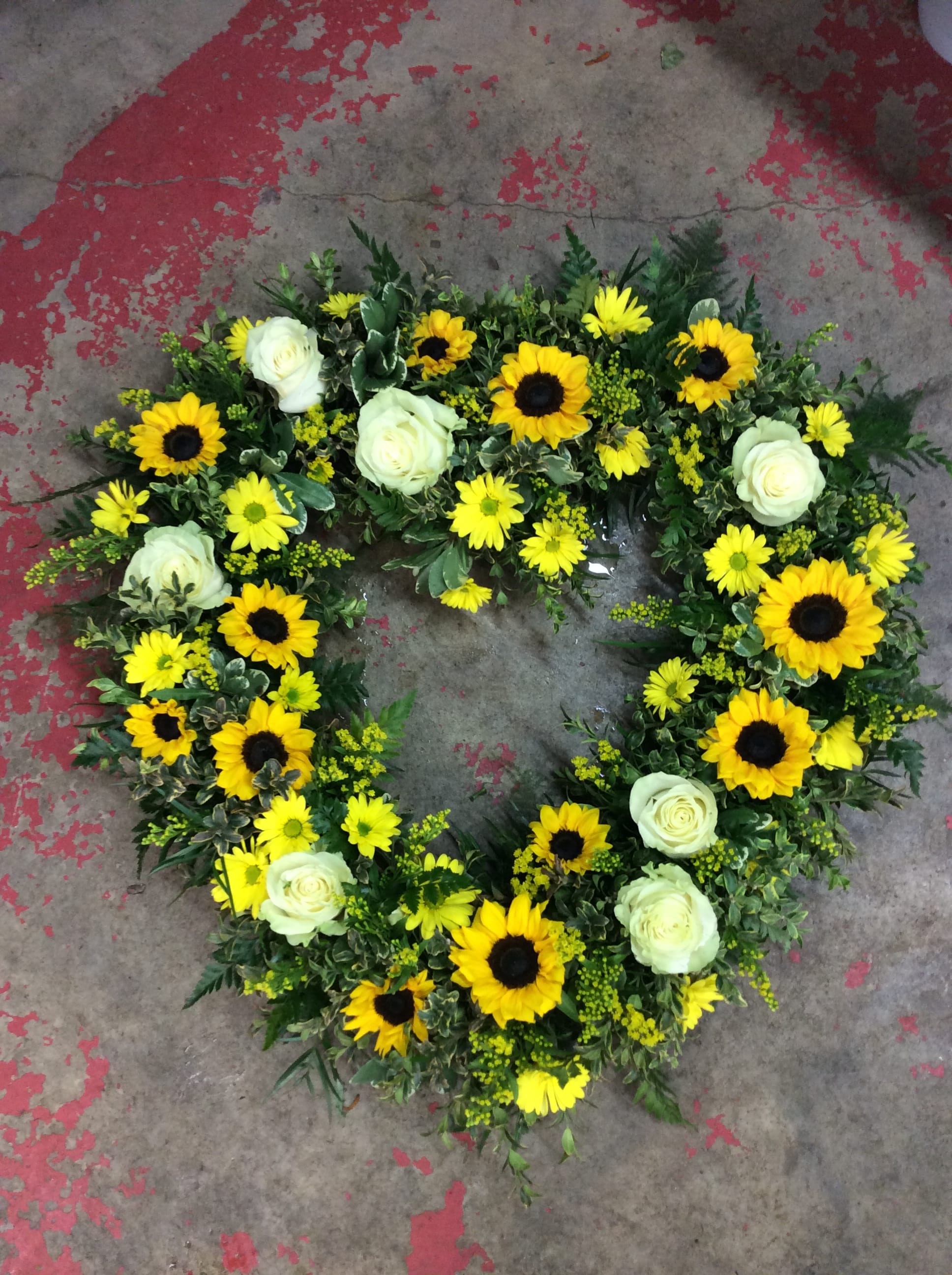 Rustic Heart - Heart shaped sympathy wreath of sunflowers, yellow daisies and white roses. Florals may vary due to availability while keeping the overall look and feel of the arrangement.  