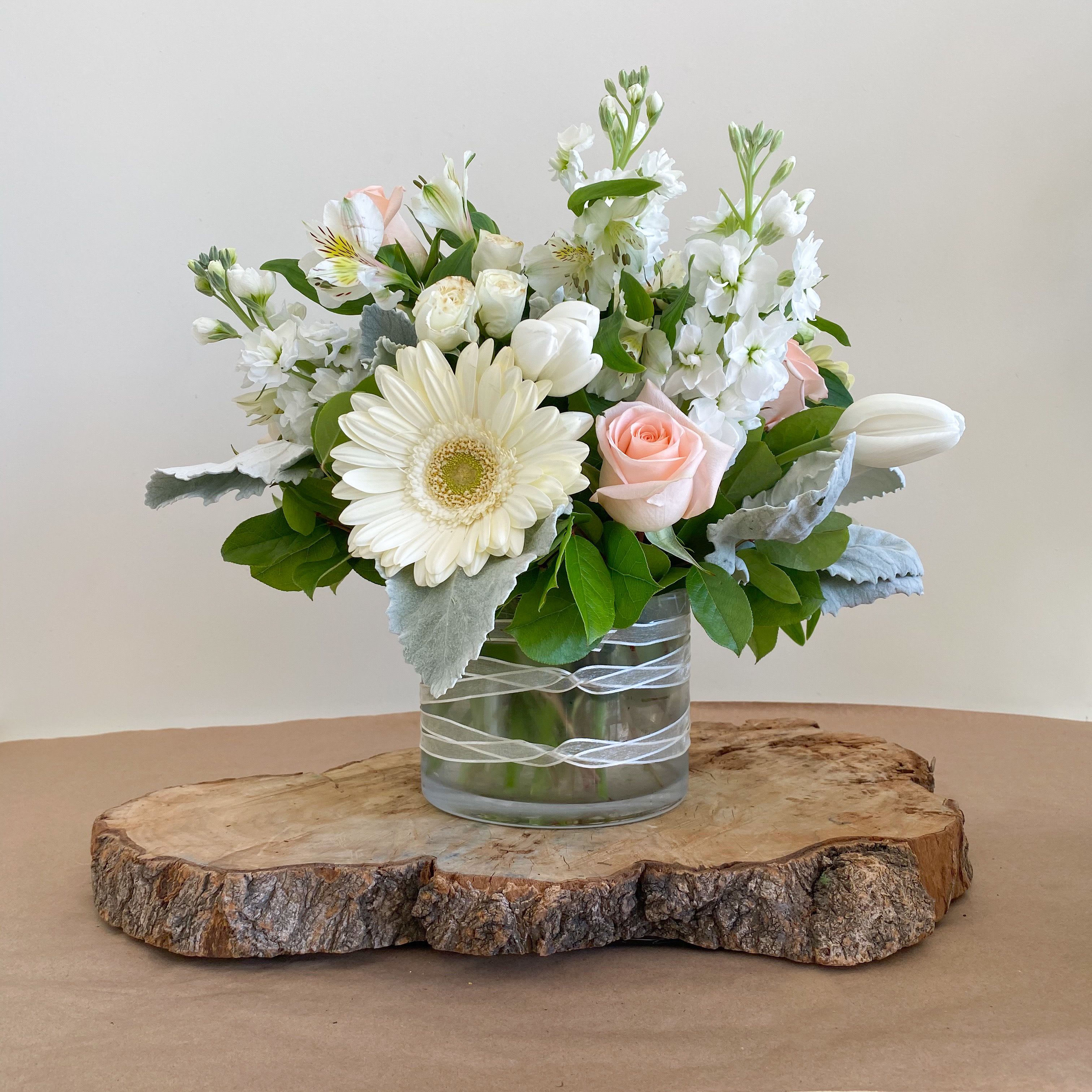Pure Pleasures Pure Pleasures - Pure Pleasures is beauty and sweet innocence come to life in this dreamy collection of pearly white and pastel blooms in a clear vase with ribbon accent This arrangement includes, Gerber Daises, Roses, Tulips, Alstroemeria, Spray Roses, Snapdragons and stock. **Please note: wood; slab under arrangement is not included** Substitution may occur Occasionally, substitution of flowers, plants, or containers may occur due to local and seasonal availability. We take the utmost care to ensure the same style and color scheme of the arrangement is maintained using similar items of equal or greater value. The Arrangement and/Vase may look different The arrangement that is delivered contains the same number of flowers but they are arranged throughout the entire vase. The vase shown may be out of stock, and we will replace it with a ;similar vase.For the arrangement the look, style and color may be different from what is pictured. Why bud stage? To ensure the freshest flower delivery, certain flowers may arrive in their bud stage. This increases your flowers’ shelf life so you can enjoy them longer. Please allow 2-3 days for the flowers to reach full bloom.