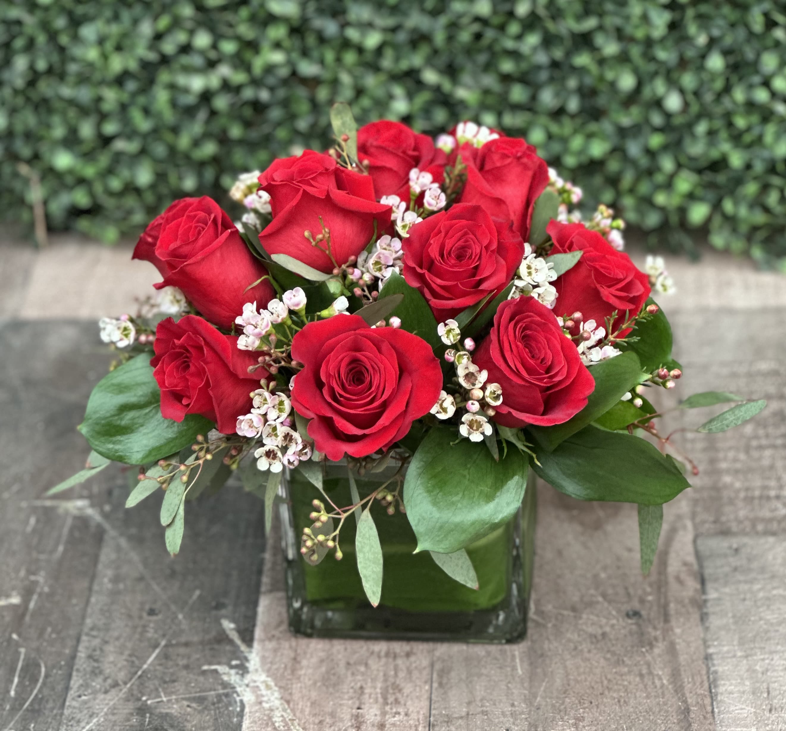 CLUSTER OF LOVE (RED) - This clustered arrangement comes designed with roses, seeded eucalyptus, wax flower and assorted greenery in a cube wrapped with a leaf.  