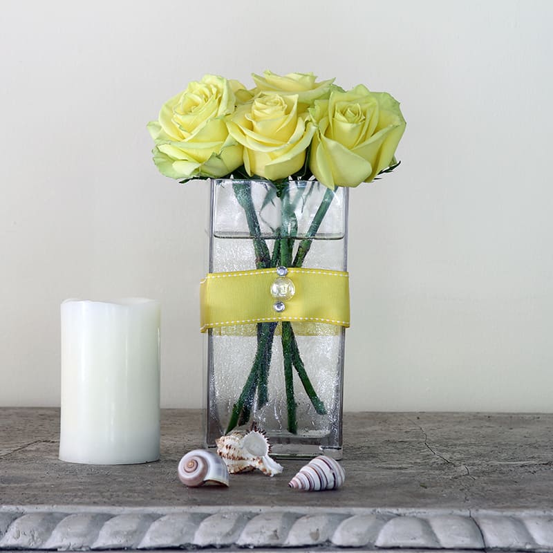 Surprises - Yellow roses in a tall rectangular clear glass vase with yellow ribbon decoration. 