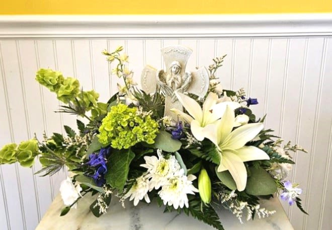 Sacred Garden Table Arrangement  - Saying goodbye is always a challenge.  Flowers are always an appropriate way to share your condolences.  This beautiful flower arrangement is white with hues of blue and a poly-resin cross with a guardian angel silhouette. approx. dimension : 17 in W X 13 in H