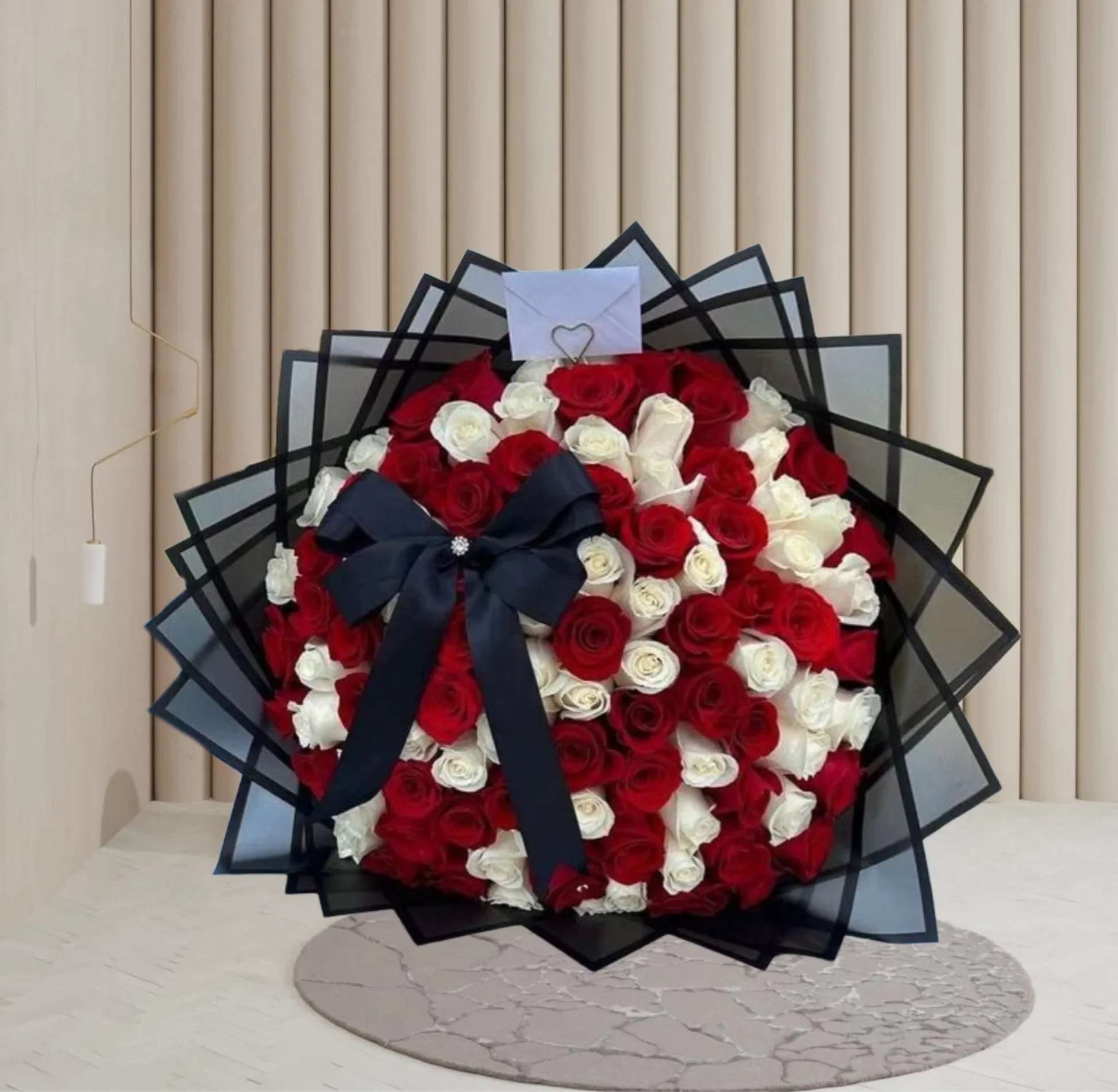 Elegant Mixed Bouquet - A luxurious round bouquet featuring a stunning mix of deep red and pure white roses, symbolizing love and harmony. Wrapped in layered black mesh paper for a modern, bold finish and adorned with a black satin bow and elegant envelope detail. Perfect for romantic gestures, anniversaries, or any moment worth celebrating in grand style.