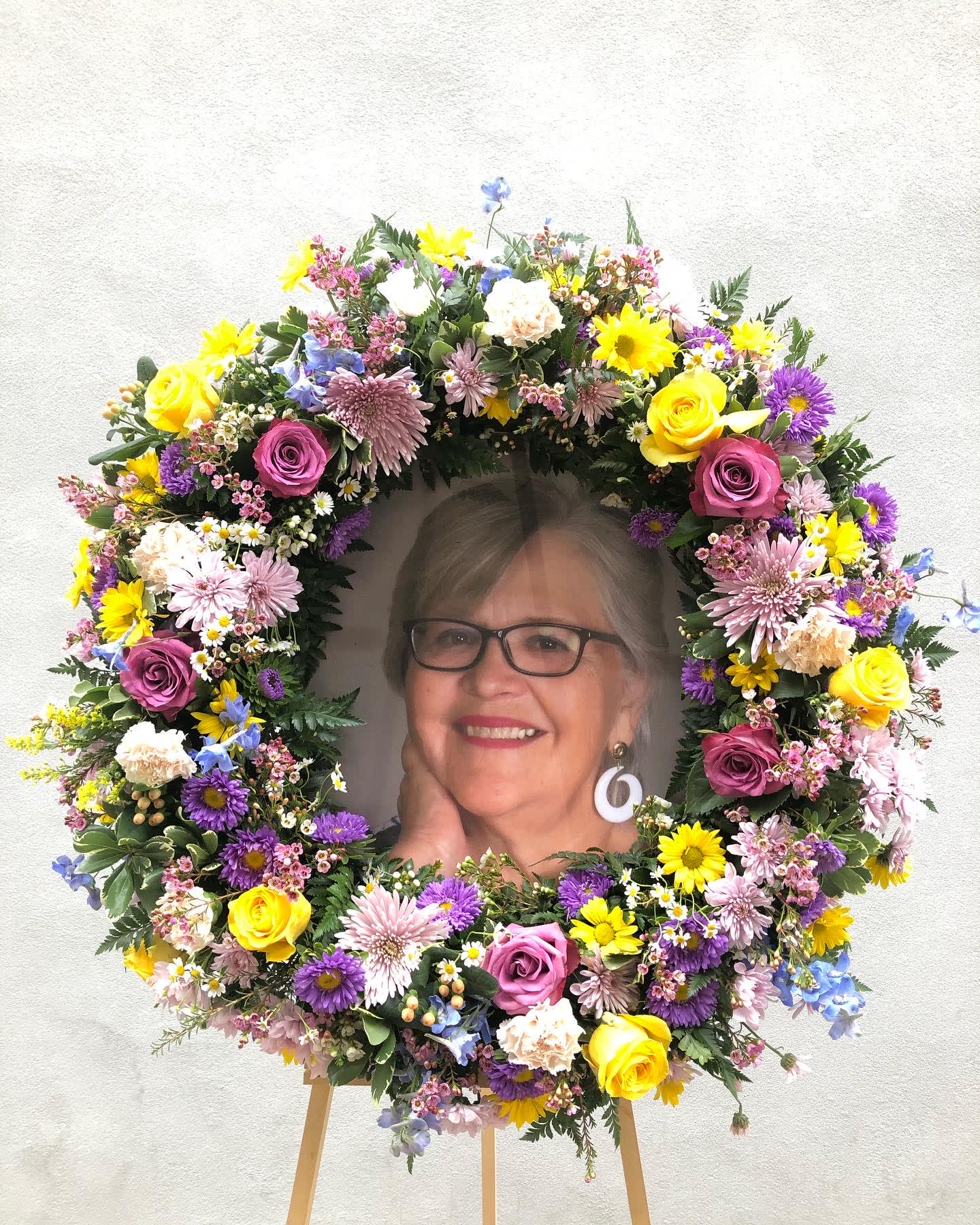 Wildflower Power Memorial Wreath - Flower wreath filled with wild flowers in lavenders, yellows, blues and pinks.  You provide the photo, and we can make sure your loved one's memory is celebrated.  Arrangement measures approx. 23in round, comes on a 6ft stand.