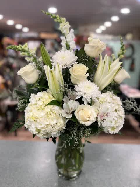 White Elegance (WE) White Elegance (WE) - An all white design is both elegant and beautiful. A clear glass vase is filled with Hydrangea, snapdragons, lilies, roses, Gerber daises and more. Flowers may differ