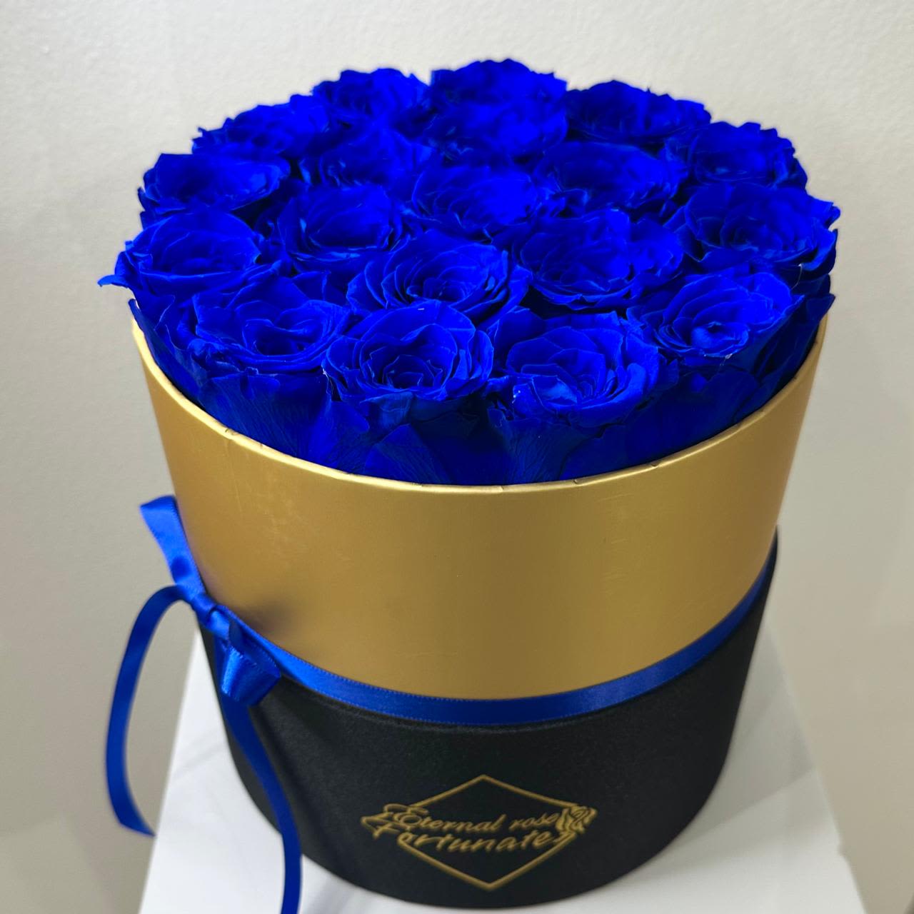 Long Lasting Blue Roses in a Round Box Medium - A round box filled with 19 rich, deep blue roses — a striking and elegant arrangement that makes a bold statement.  Real roses that have been carefully treated to maintain their fresh look for months or even years. These everlasting blooms are perfect for expressing timeless love, passion, and elegance. No watering or maintenance required — just lasting beauty.