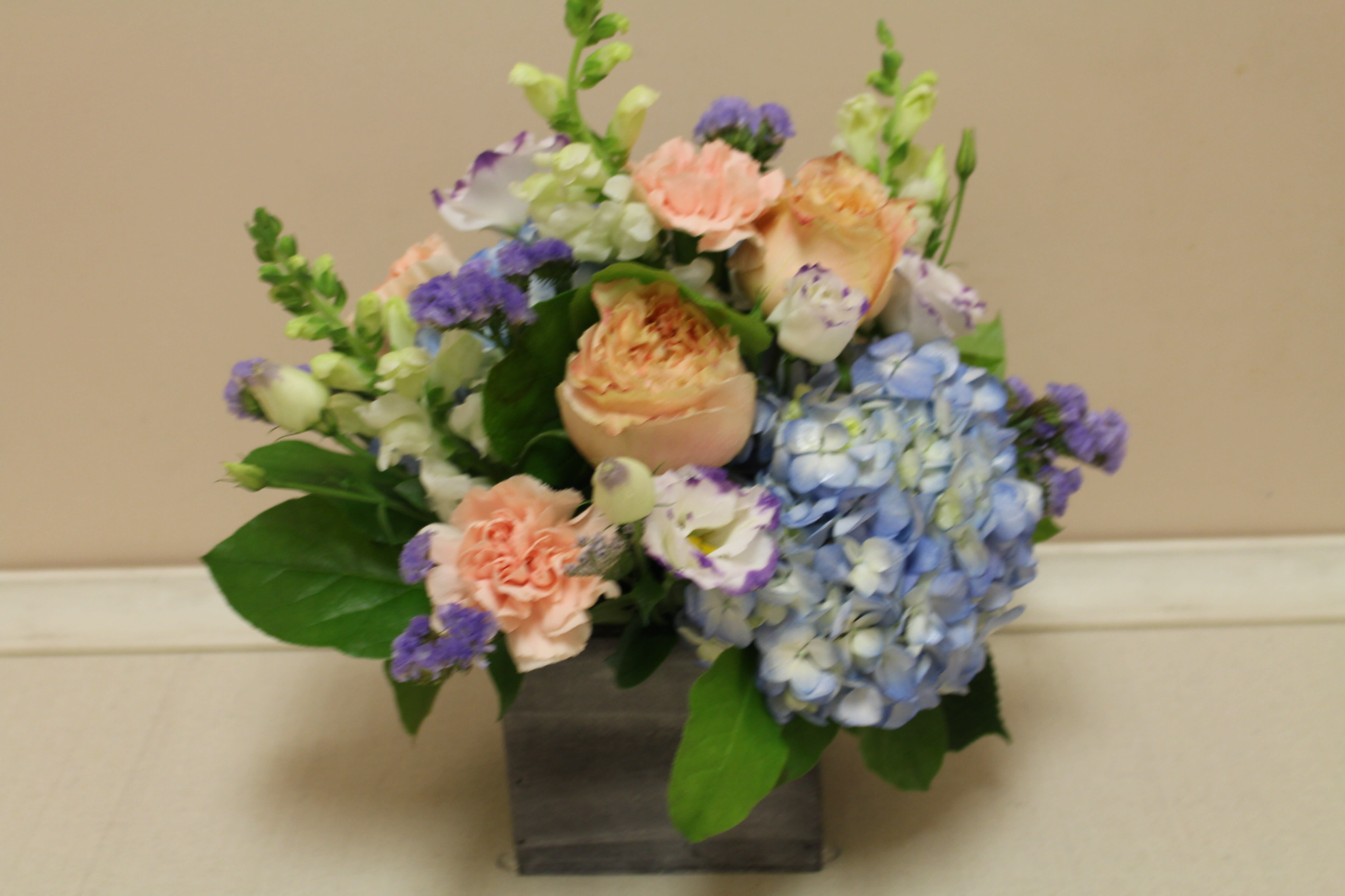 garden whisper - a delicate arrangement, soft peaches and blues in a twig based basket.  Straight out of a walk in the woods.  