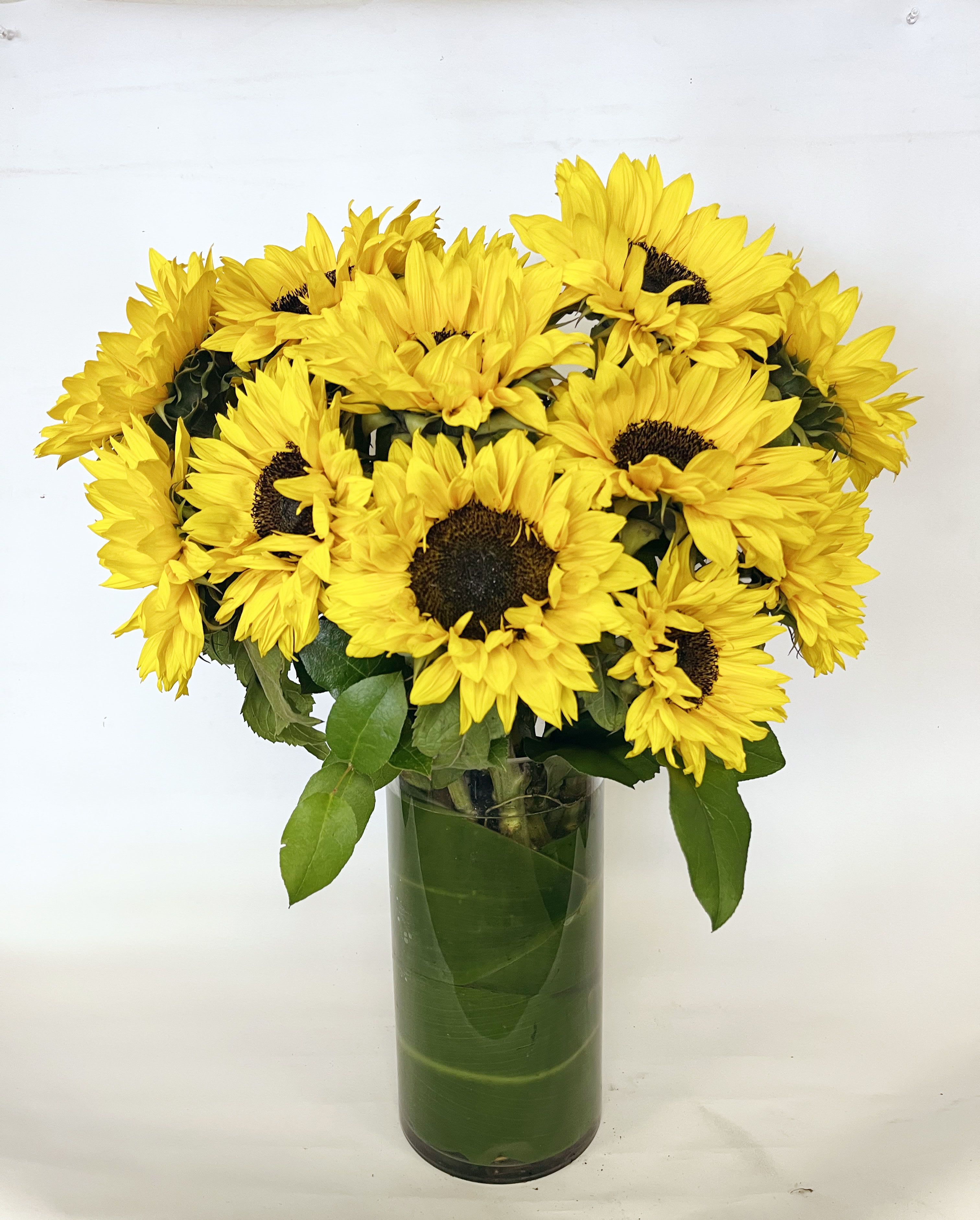 SUNFLOWER TOWER - TALL VASE OF SUNFLOWERS WRAPPED IN GREENERY. 