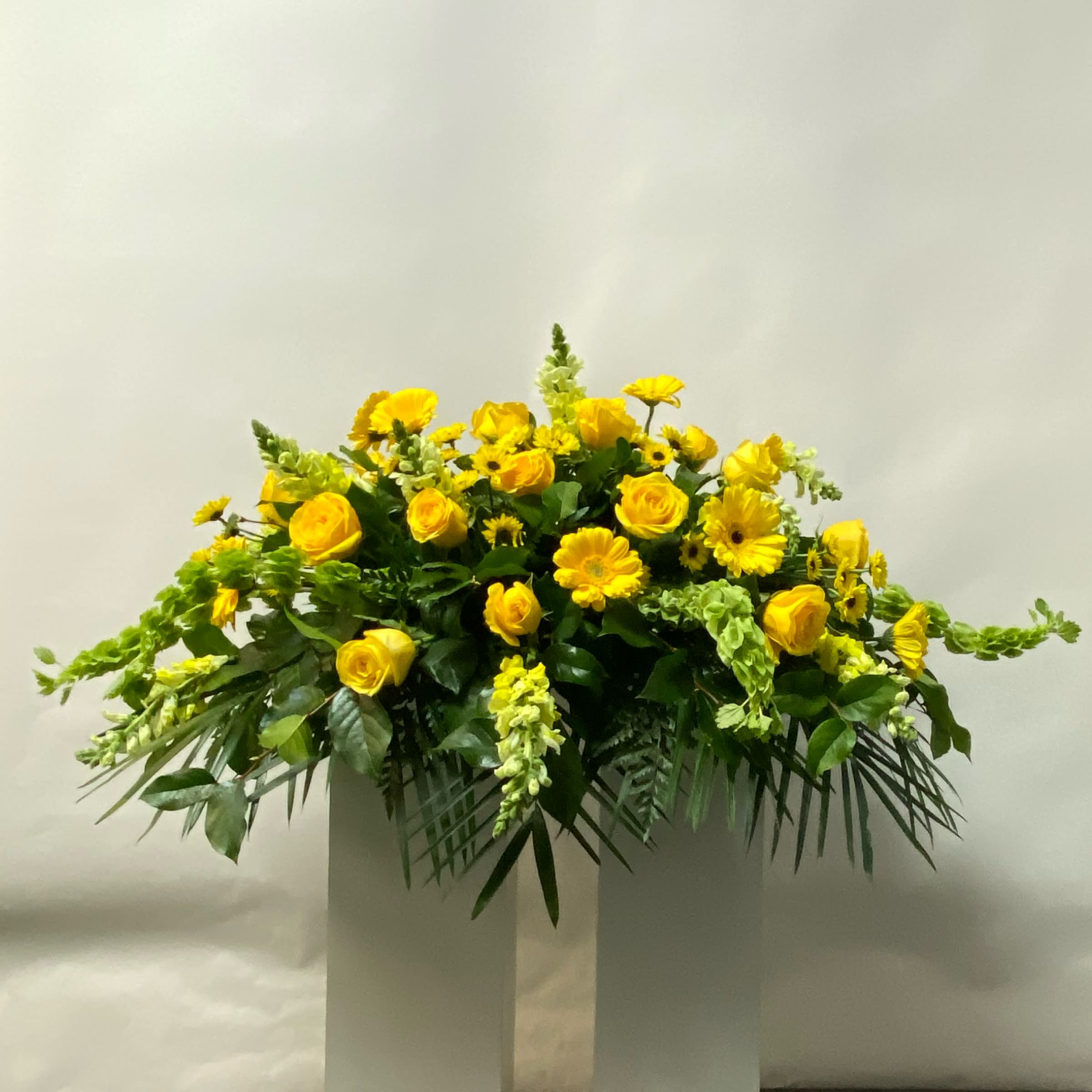 Golden Gardens Casket Spray - This Casket Spray includes Yellow Roses, Yellow Gerbera Daisies, Bells of Ireland, Yellow Snapdragons, and Viking Pomps. Or as Similar as Possible. 