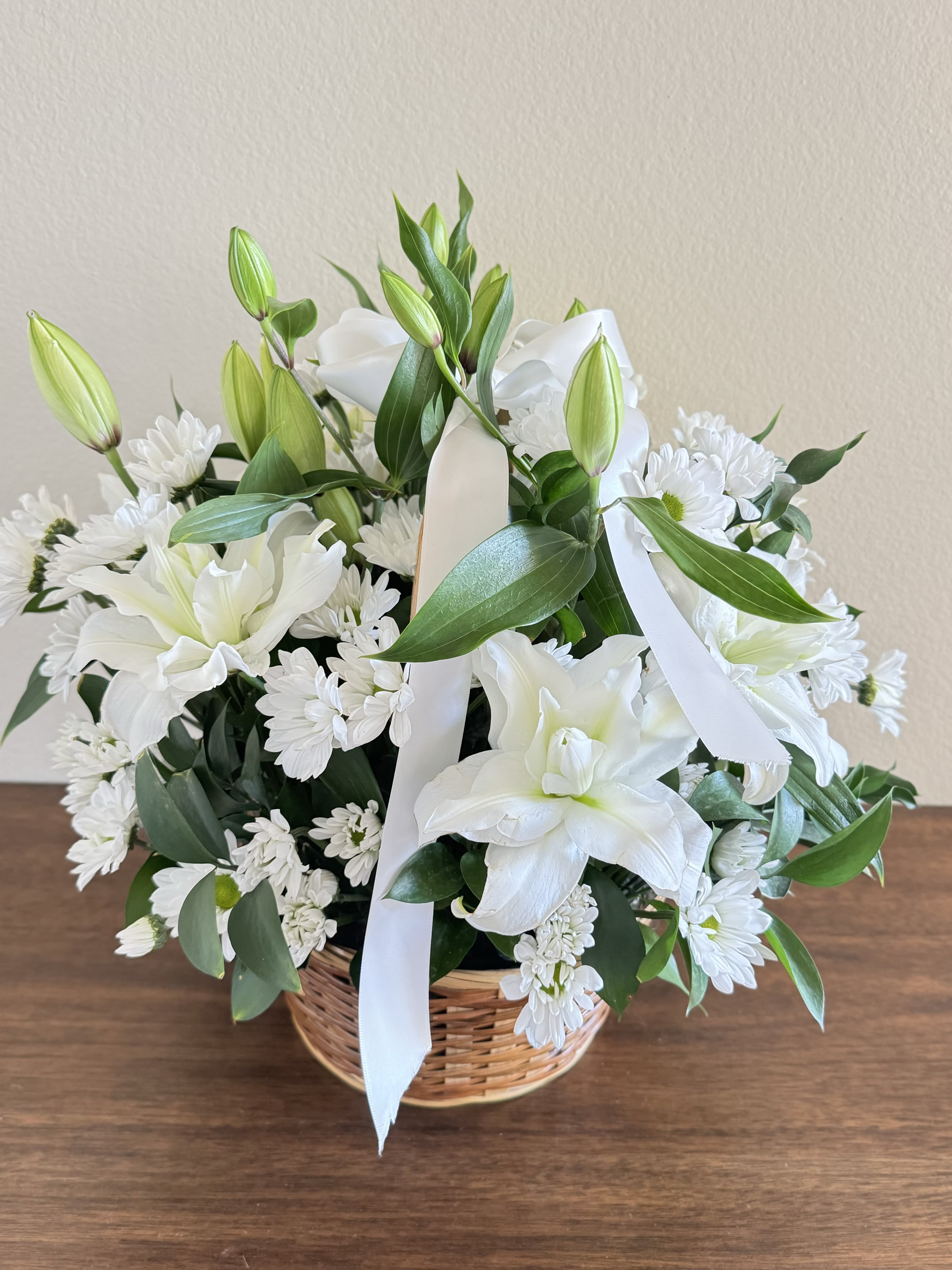 Flower in a Basket &quot;Serene Comfort&quot; - This elegant funeral flower basket is a heartfelt tribute, featuring the serene beauty of lilies and the comforting presence of chrysanthemums. The delicate white lilies symbolize peace and purity, while the vibrant chrysanthemums convey a message of eternal love and remembrance. Arranged thoughtfully, this floral arrangement brings comfort and elegance during times of loss. Perfect for honoring a loved one, this funeral flower basket offers a graceful way to express sympathy and respect. Available for flower delivery in Los Angeles and surrounding areas, this beautiful arrangement provides solace and beauty in moments of sorrow.