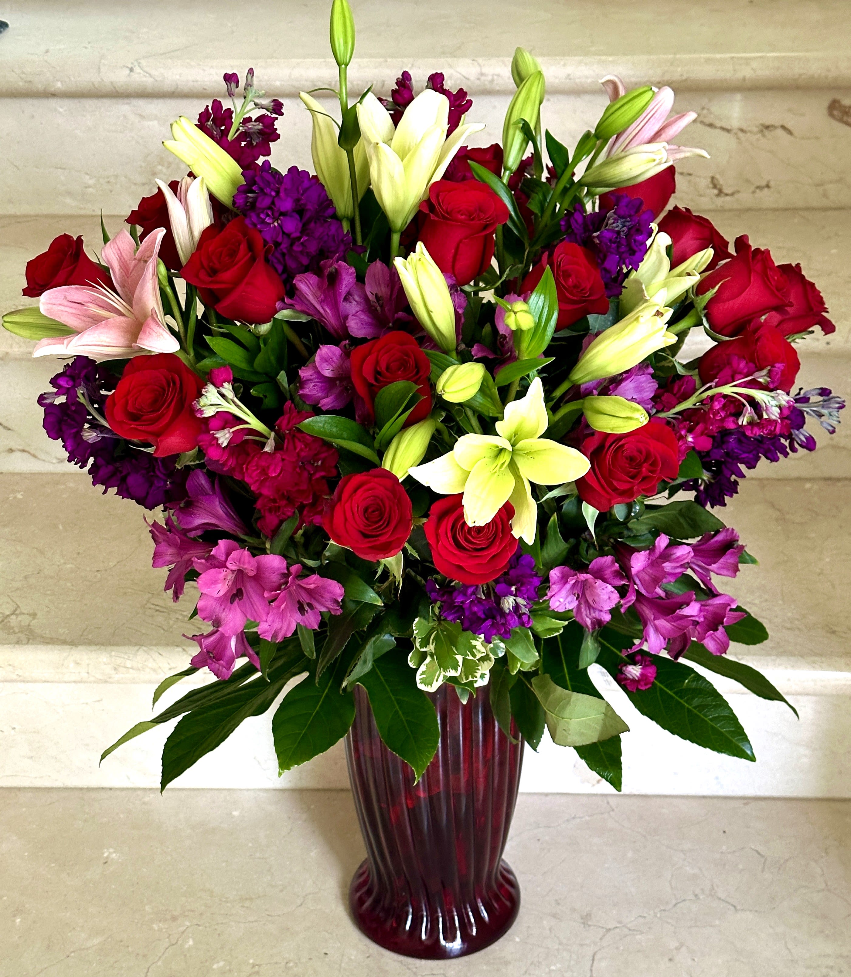 Dark Sensation - A mixture of Premium flowers with Roses, Lilies, Stock, Astro and more with Greenery in a stylish glass vase.