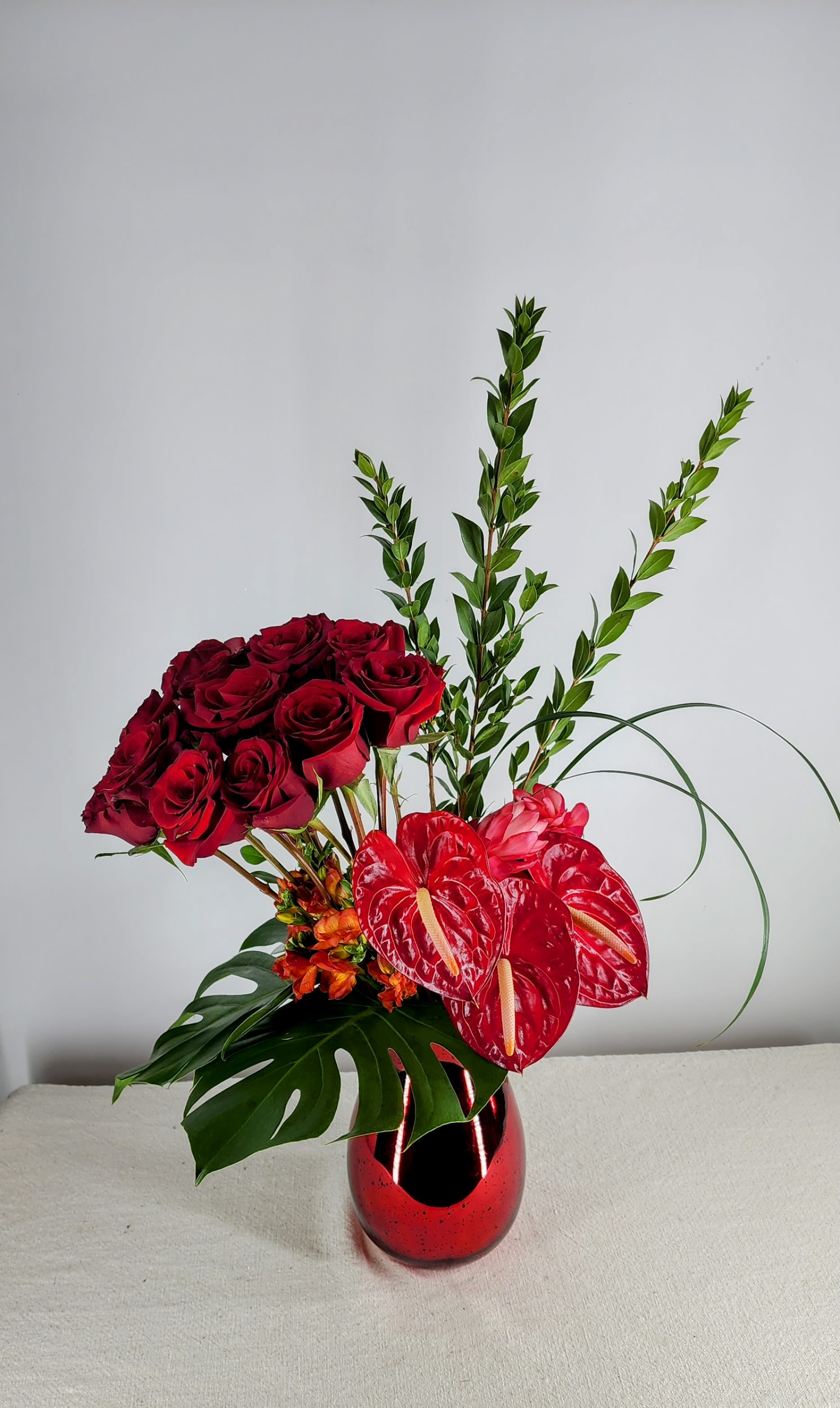 Contemporary Rose  &amp; Anthurium Arrangement - This arrangement is designed with a dozen freedom roses, tropical Anthurium, &amp; Monstera leaves in a fabulous red mercury vase.