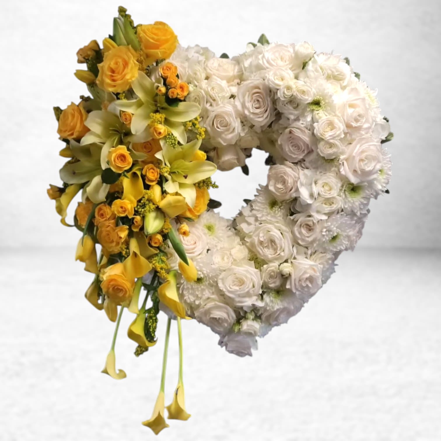 Golden Embrace Heart Tribute - The Golden Embrace Heart Tribute is a stunning heart-shaped standing spray designed to honor a life filled with warmth and love. Featuring a base of elegant ivory roses, white hydrangea, and chrysanthemums, the design is beautifully accented by a cascade of golden yellow roses, calla lilies, and Asiatic lilies for a radiant finish. This heartfelt display symbolizes eternal love and remembrance, making it a meaningful centerpiece for funeral services and memorials.  Delivery is available to funeral homes across Galveston, League City, Texas City, Dickinson, and the southern Houston region. Whether you're commemorating a loved one in Hitchcock, La Marque, or Friendswood, this sympathy arrangement brings comfort and grace in a time of loss.  Substitution Policy: We strive to deliver each arrangement as pictured. However, due to seasonal availability and local market conditions, certain blooms or colors may need to be substituted. If specific flowers (such as calla lilies or spray roses) are unavailable, we will replace them with comparable varieties of equal or greater value while maintaining the design, color palette, and overall integrity of the tribute. Substitutions are made with great care and respect, ensuring the sentiment remains beautifully expressed.