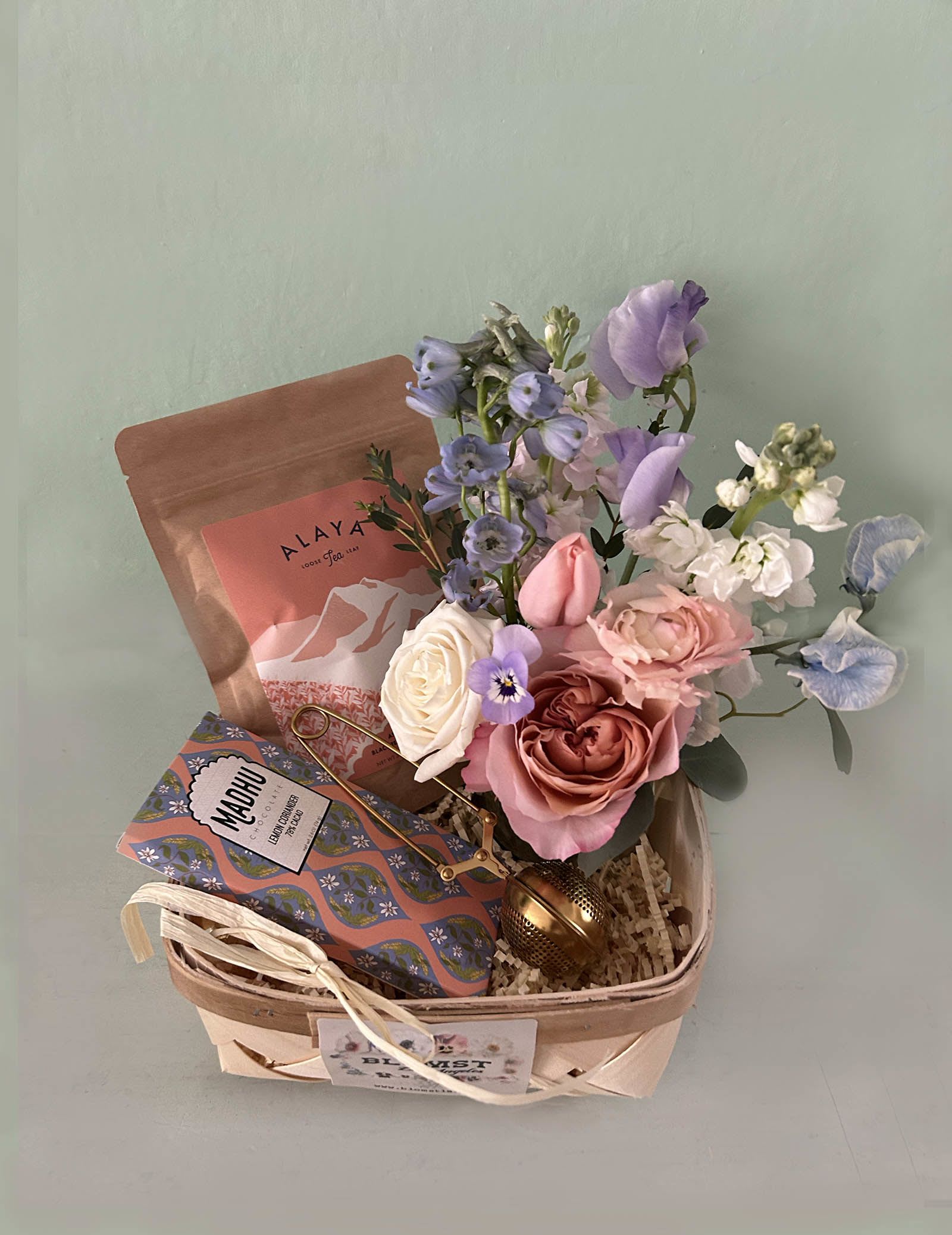 Violet Vegan Box - The pretty Blomst LA qift box is full of lovely tea &amp; vegan chocolate, and a tea infuser. It is adorned with a small fresh Blomst flower arrangement. Ginger Assam Tea - a simple combination of black tea and ginger. A biodynamic Assam black tea blended with organic ginger that is grown in the gardens of the women who pluck the tea. Organic and regenerative tea, sourced directly from people and planet-friendly Indian farms. Lemon Coriander chocolate bar - 78% Cacao, Palo Santo sticks and a cute mini vase of Blomst signature flowers all in white colors. All placed in a woven wooden basket (7 by 7 by 4).