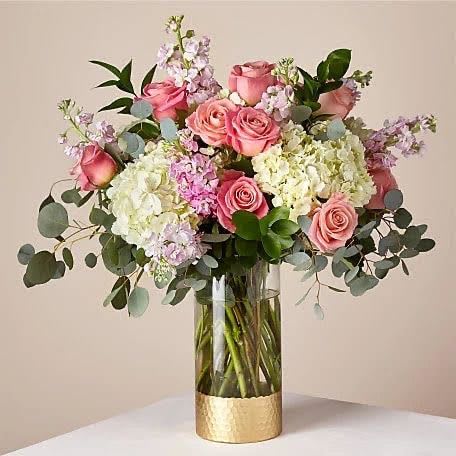 Elegant Floral Bouquet Elegant Floral Bouquet - Add a touch of sophistication to any room with our stunning Elegant Floral Bouquet. This exquisite arrangement showcases a harmonious blend of pink roses, white hydrangeas, and delicate purple flowers, all carefully selected to create a visually appealing display. The clear glass vase with a gold base adds a luxurious finish, making it perfect for special occasions or as a thoughtful gift. The bouquet is presented on a crisp white table against a soft beige background, highlighting its beauty and elegance.