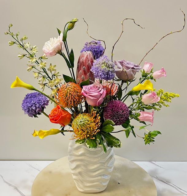 Pearl Crush - A vibrant and elegant arrangement designed to turn heads. Featuring a bold mix of colorful blooms in a sleek, pearl-toned ceramic vase with a raffled texture—this piece is full of personality and style! Approx. size 13&quot;x20&quot;