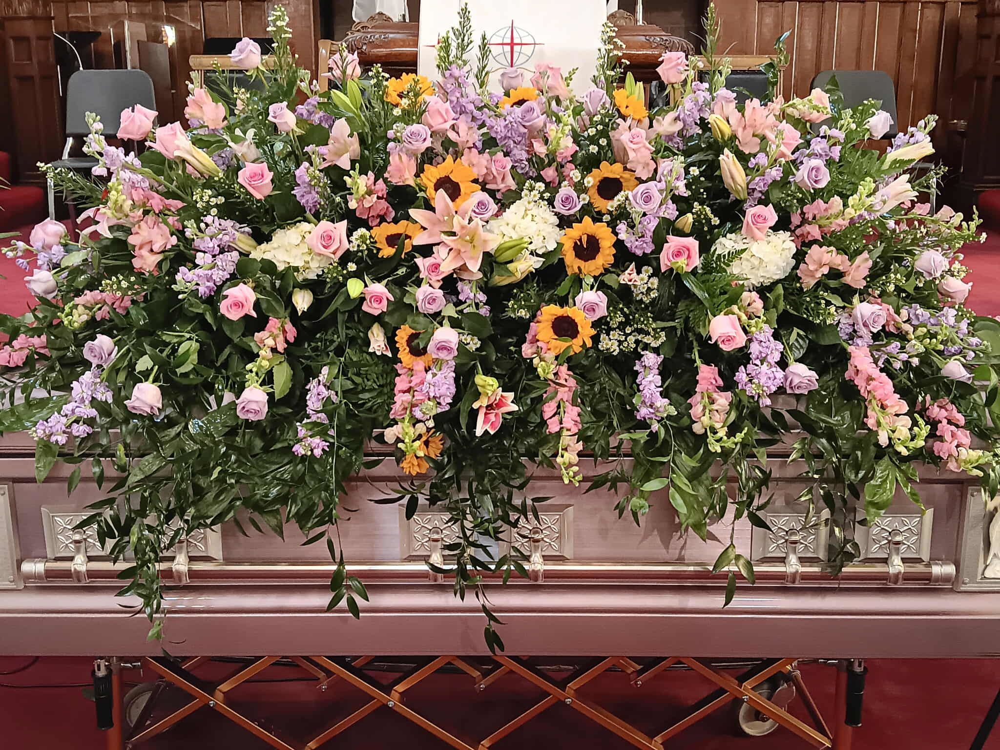 Full Casket Cover (Spring Colors) - This beautiful full casket cover comes with lavender and pink roses, stock, white hydrangeas, sunflowers, pink lilies, babies breath and lush greenery to tie it all together.    *Flowers can be substituted to different colors or flowers price is subject to change*  
