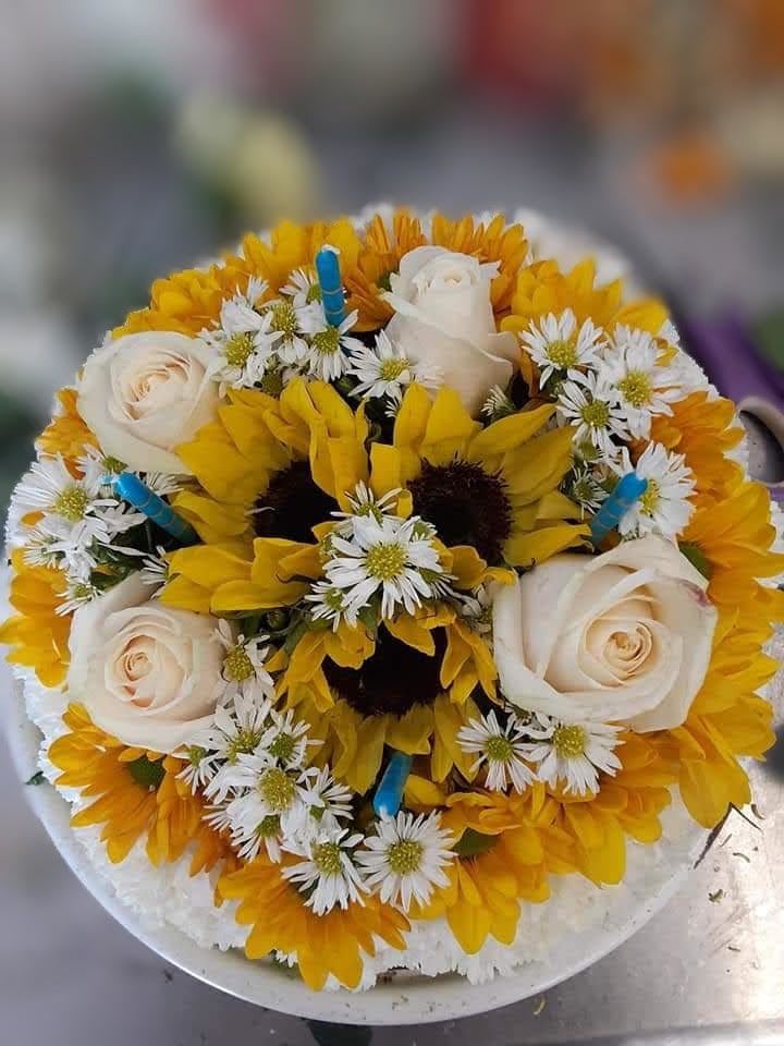 Sunny Bright Flower Birthday Cake - Celebrate with a slice of sunshine! This delightful floral cake is artfully crafted from bright sunflowers, cheerful yellow daisies, classic white daisies, fluffy carnations, and delicate white Monte Cassino asters. Arranged to resemble a real birthday cake, it’s topped with festive candles and presented on a sturdy glass or ceramic plate. A joyful and unforgettable centerpiece—no baking needed, just fresh blooms and big smiles!