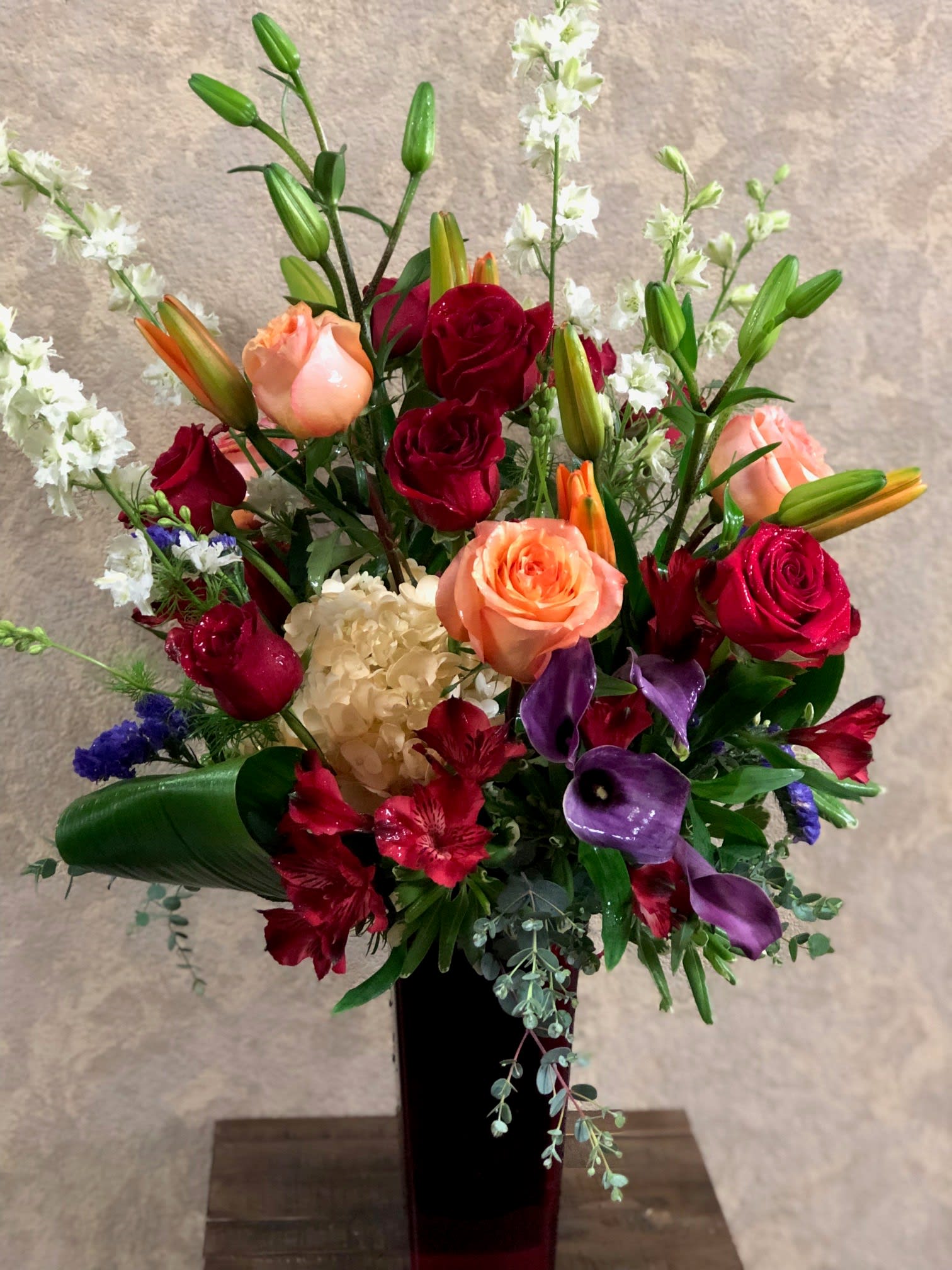 Copenhagen - Copenhagen is full of romantic colors that says it all!  Type of Flowers: Red and Orange Roses, Orange Lilies, White Hydrangea, Purple Calla Lilies, White Larkspurs, and Red Alstroemerias in a tall red vase. Availability: All year round Substitute Available: Yes Design View: All-sided Facing View Photo shown: Regular