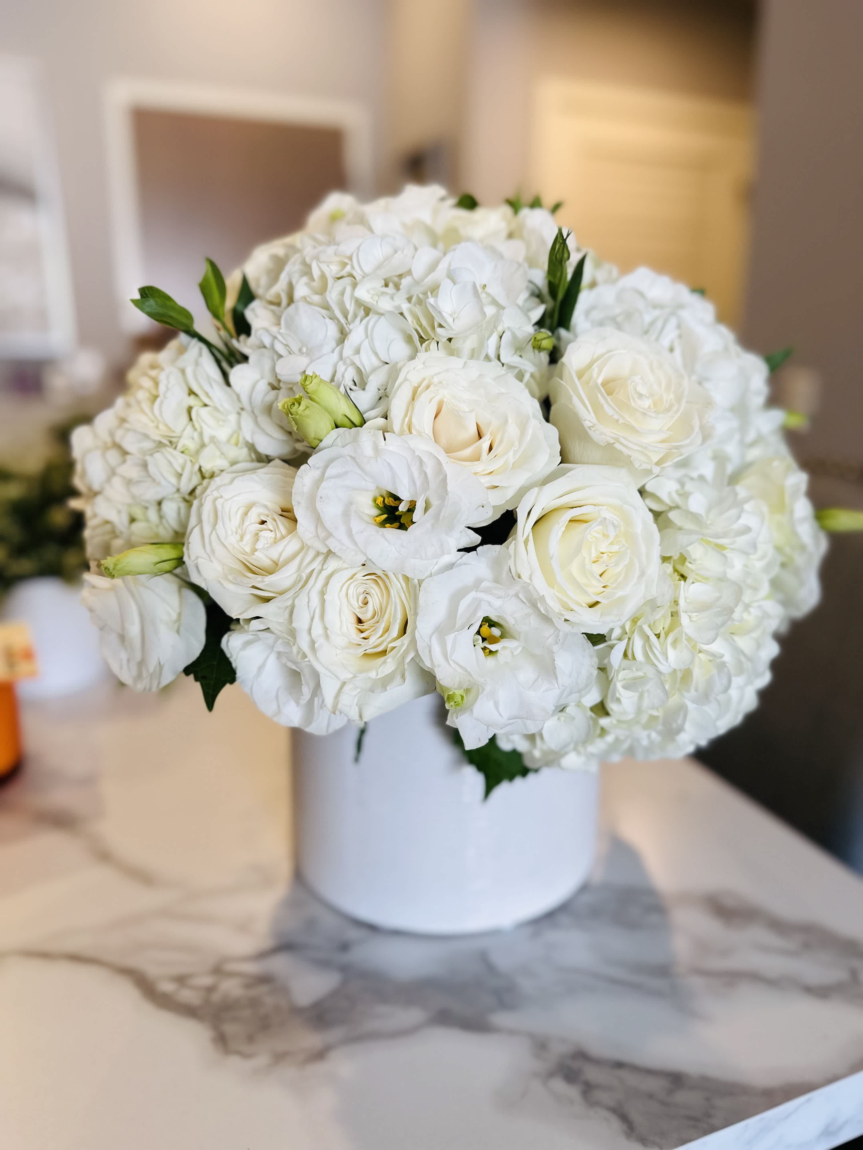 Pure Blossom Bouquet Pure Blossom Bouquet - A luxurious, monochromatic arrangement featuring white hydrangea, ivory roses, and white lisianthus, tightly designed in a sleek white ceramic cylinder vase. The clean, dome-shaped silhouette and soft ivory tones create a timeless and sophisticated statement, perfect for any occasion that calls for elegance and grace. Ideal for weddings, sympathy arrangements, thank-you gifts, or upscale interior styling, this premium white bouquet brings freshness and serenity into any space. Available for same-day flower delivery throughout Los Angeles, including Beverly Hills, Century City, Brentwood, and West Hollywood.