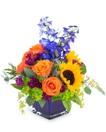 Summer Blooms Summer Blooms - A beautiful blue cube vase filled with summer blooms sunflowers , roses, delphiniums designed in a cube vase. Enjoy these summer nights with this summer blooms.