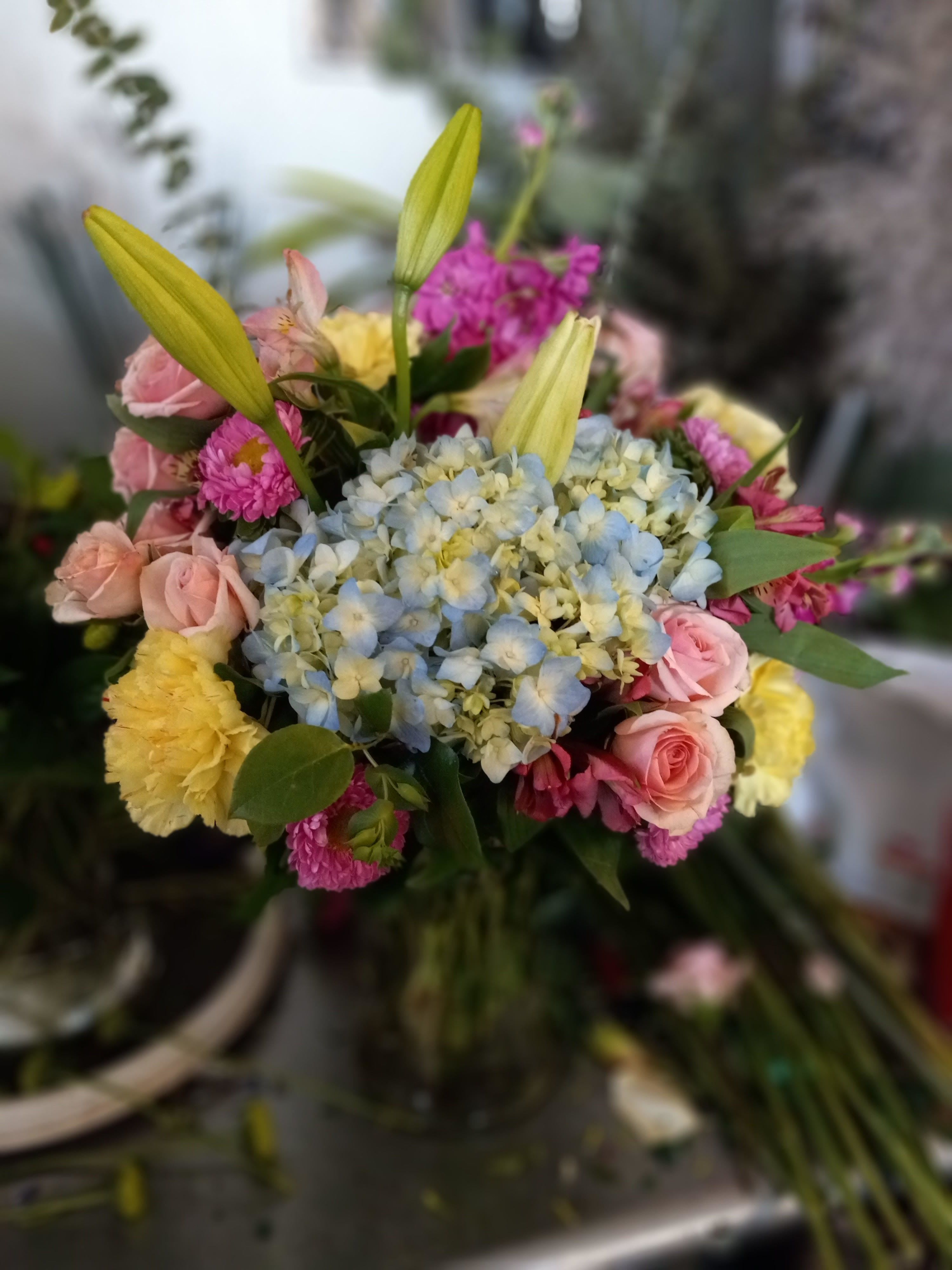 beautifully enchanted - Graceful and full of soft color, Enchanted Beauty is a bouquet that radiates warmth and elegance. A dreamy blue hydrangea creates the perfect focal point, surrounded by cheerful yellow carnations and romantic pink roses. Pink spray roses and fragrant pink stock add lush texture and a gentle sweetness, while pink alstroemeria and fresh, flowing greenery complete the design with natural charm. This arrangement is perfect for celebrating life’s tender moments with beauty that feels both magical and heartfelt.
