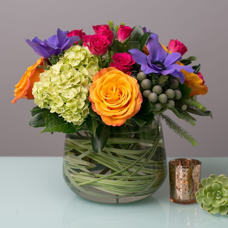 The Bright &amp; Cheerful - A beautiful clear glass cylnder vase lined with bear grass filled with a creative combination of colorful seasonal flowers. 