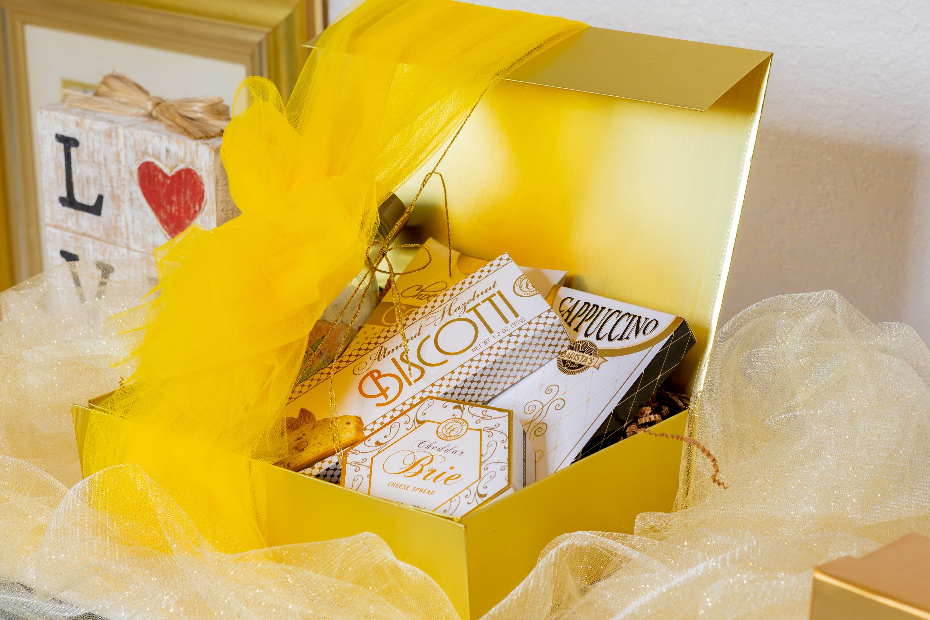 Golden delight - A stunning golden box filled with gourmet treats like biscotti, cappuccino, and cheese spread, wrapped with elegance and perfect for special occasions.