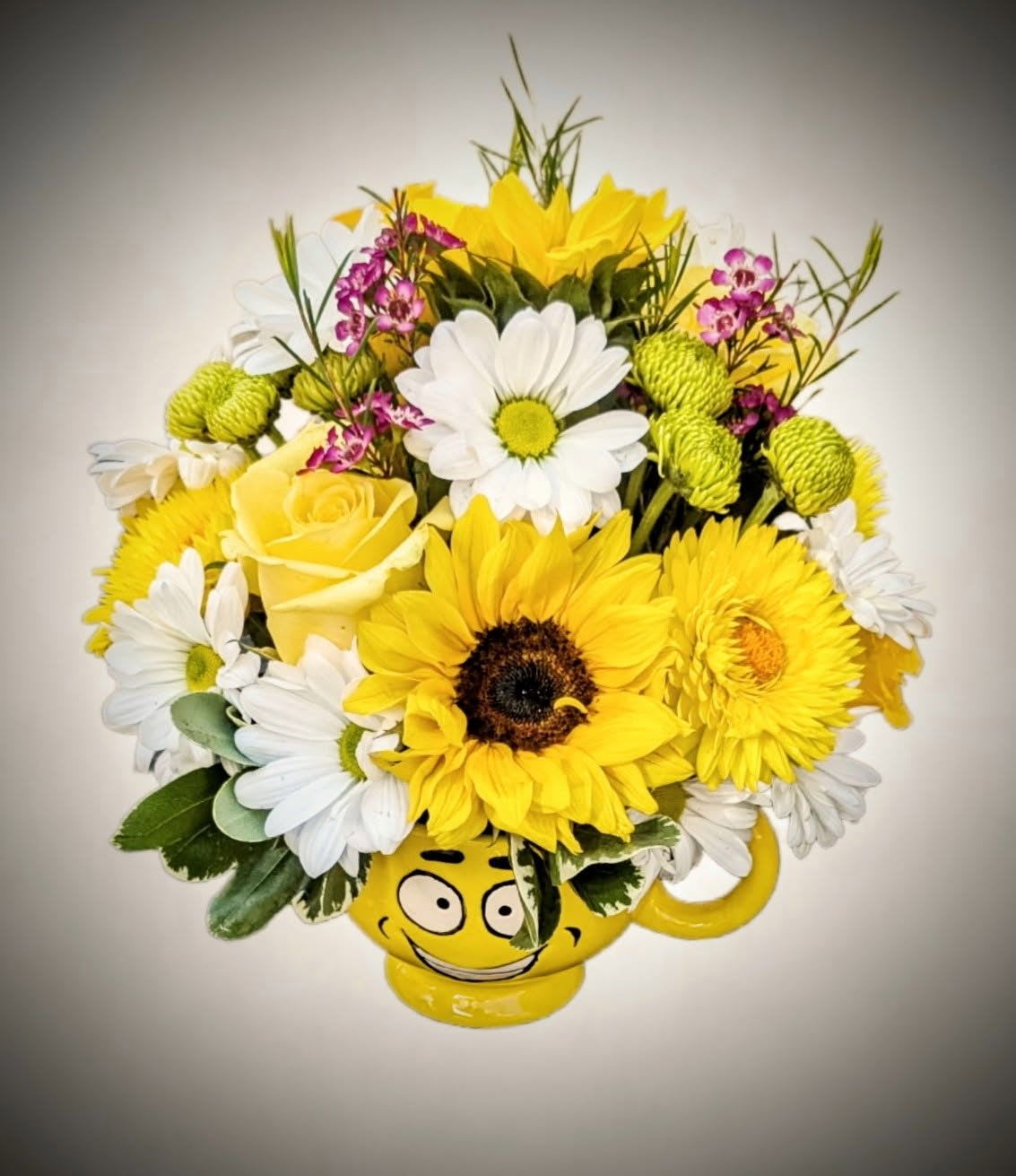 Sunshine Smile Bouquet Sunshine Smile Bouquet - Brighten someone’s day with our delightful Sunshine Smile Floral Arrangement! This vibrant bouquet bursts with the warmth of yellow sunflowers, golden roses, cheerful daisies, lush green button poms, and sprigs of purple waxflower — all artfully arranged in a fun, smiley-face ceramic mug. Perfect for birthdays, get-well wishes, or just because, this arrangement brings joy, color, and a bit of whimsy to any space. And once the flowers have had their moment, the reusable smiley mug adds lasting charm to your desk or kitchen. Features: Fresh seasonal blooms in yellow, white, green. Playful smiley-face ceramic mug container (reusable!) Ideal for gifting or brightening up your own space Let happiness bloom — one smile at a time