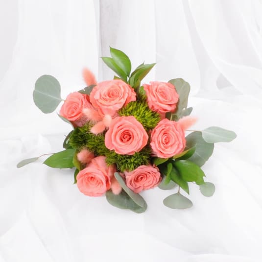 Bouquet of peach roses with green button flowers arranged on white fabric