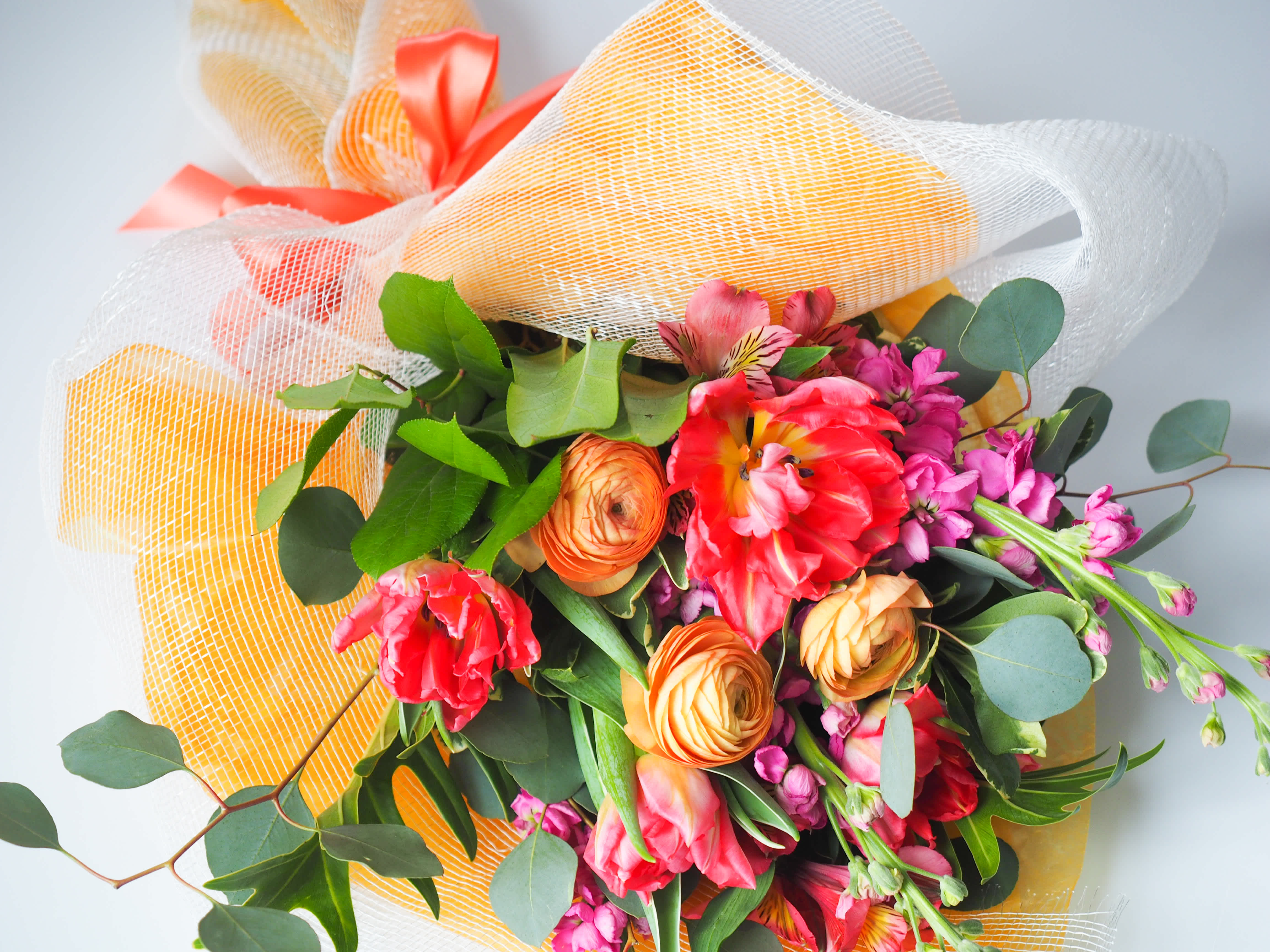 Cora - This hand-tied bouquet features a vibrant mix of blooms with special meanings. In the language of flowers, tulips symbolize &quot;perfect love&quot;, stock means &quot;lasting love&quot;, ranunculus &quot;radiant charm&quot;, and alstomeria stands for &quot;devotion&quot;.   The Cora Bouquet is wrapped in colored paper, decorative fabric and tied with double-faced satin ribbon. Flowers are delivered in water tubes so they will stay hydrated for hours until the recipient transfers flowers to a vase.  