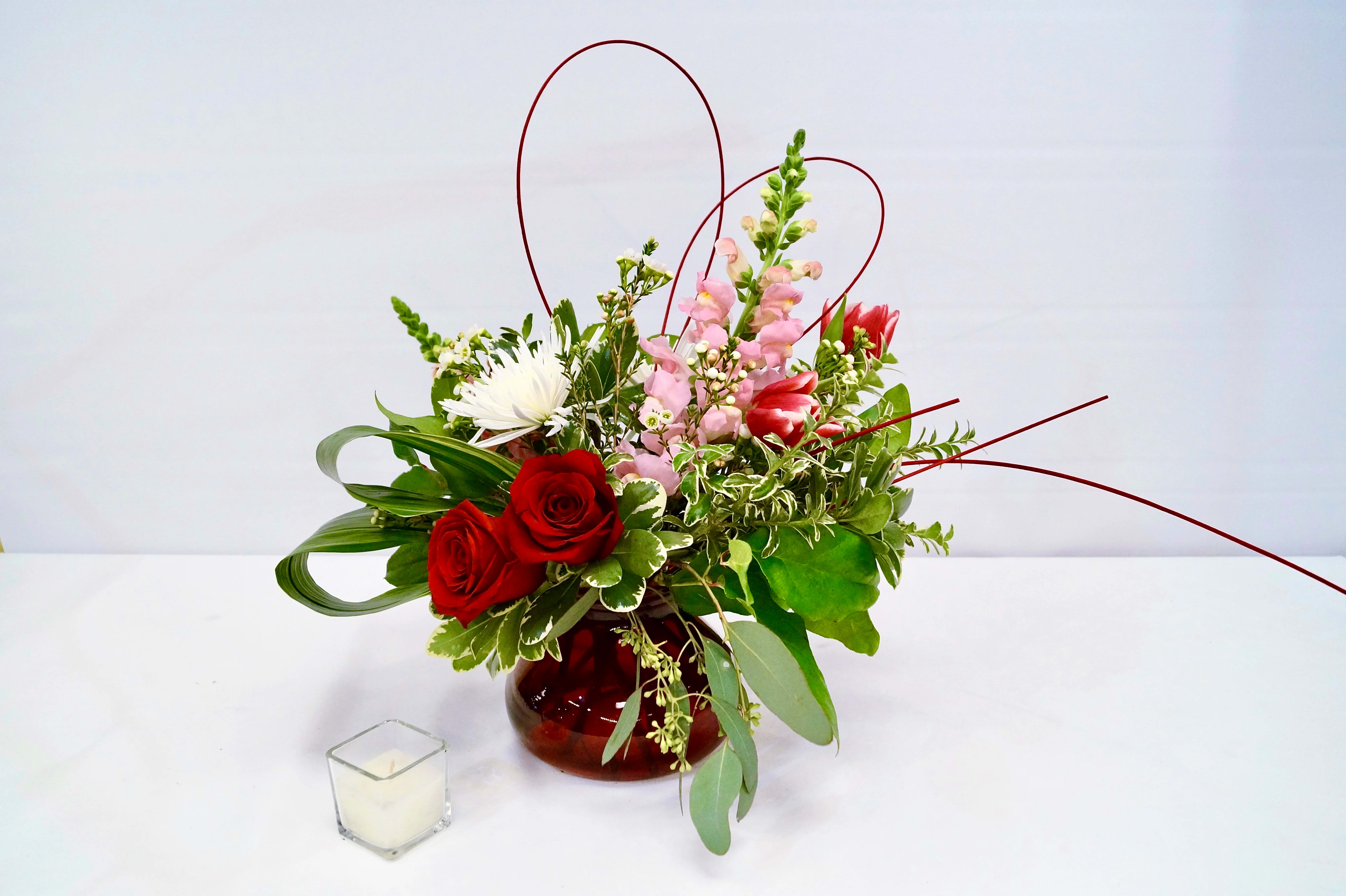 Ruby - Expressive. Vibrant. Joyful.  Express your love with our contemporary styled arrangement, designed in a Valentine's Day palette. The Ruby is a full design that features soft pink snapdragons, bi-color tulips, romantic red roses, ultramodern folded aspidistra leaves, and finished with a medelino heart. Arranged in a ruby red vase.