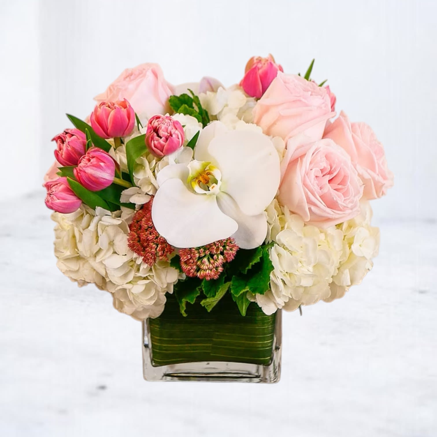 Rosé All Day Rosé All Day - Rosé All Day is a charming blend of romance and refinement—perfect for sending love, celebrating milestones, or brightening someone’s day in Galveston, League City, and surrounding South Houston communities. Featuring soft blush roses, playful pink tulips, creamy white hydrangea, and a single pristine phalaenopsis orchid, this compact design delivers elegance in a modern glass cube lined with tropical greenery. Its delicate palette and lush, textured blooms make it an ideal floral gift for birthdays, baby showers, anniversaries, or just because. Substitution Policy: Due to seasonal and market availability, certain flowers like Phalaenopsis orchids or tulips may be replaced with similar blooms of equal or greater value to maintain the look, color palette, and premium quality. The cube vase may also vary slightly in finish or lining but will always maintain a compact, low profile and clean aesthetic.