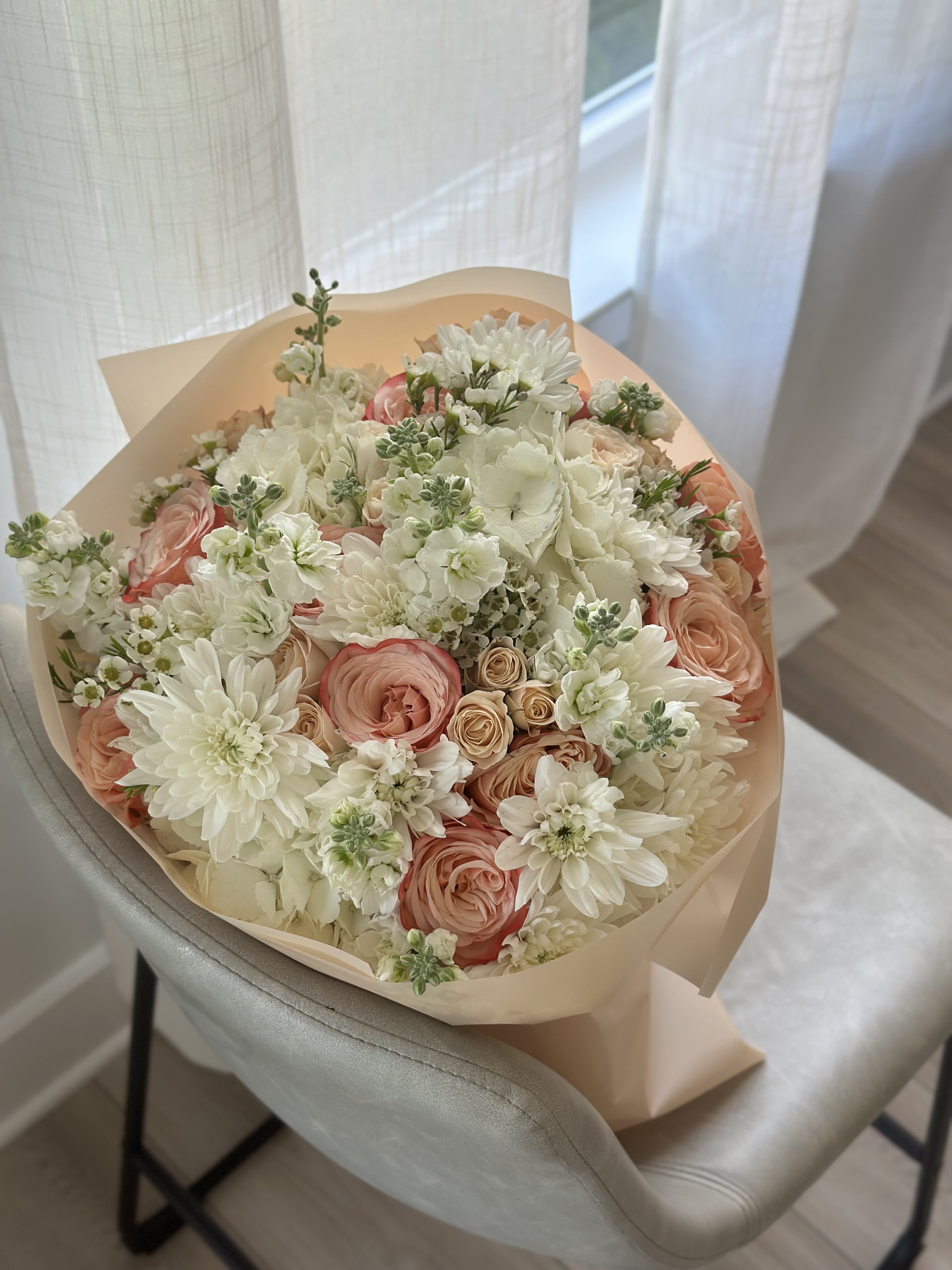 Peach Glow - A luminous bouquet of creamy dahlias, soft hydrangeas, peach and blush garden roses, and delicate seasonal greens. This radiant composition captures the warmth of a sunny morning and the elegance of a gentle smile — ideal for joyful occasions or just because. 
