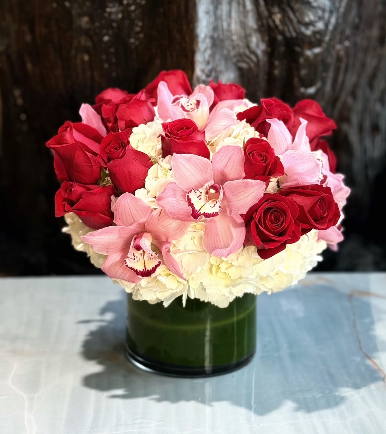 Candy - Roses, Hydrangeas, and Cymbidium Orchids in a glass vase. 